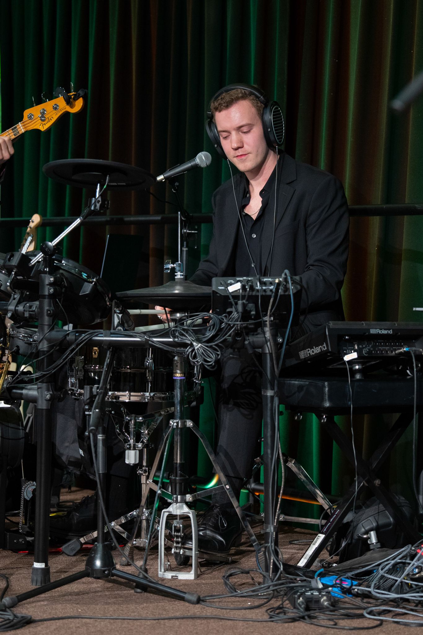Drummer performs with electronic drum kit and headphones in dark lighting.