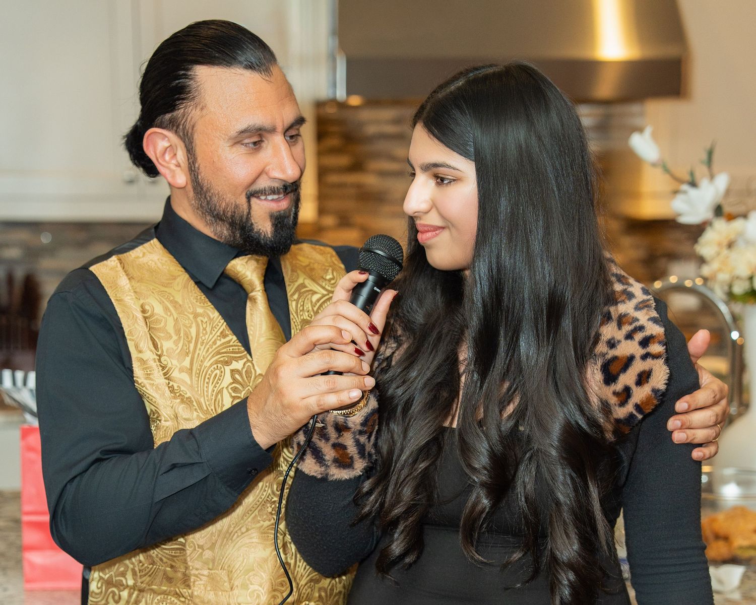 A couple shares an intimate moment during a celebration event, with the man wearing a gold and black traditional outfit.