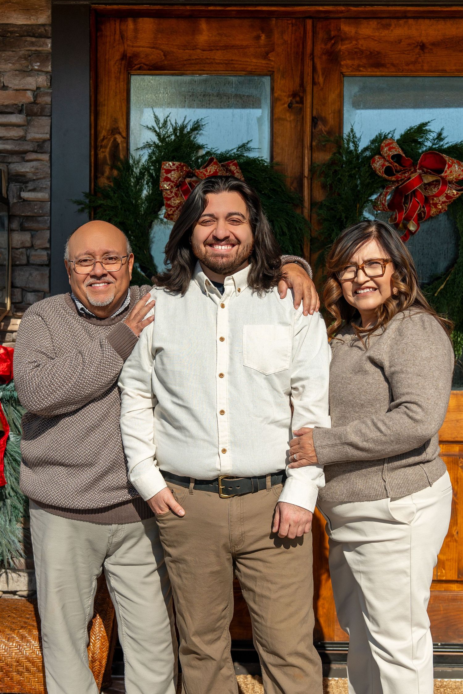 Family group photo showing people in coordinated outfits of white shirts and grey sweaters against a stone wall.