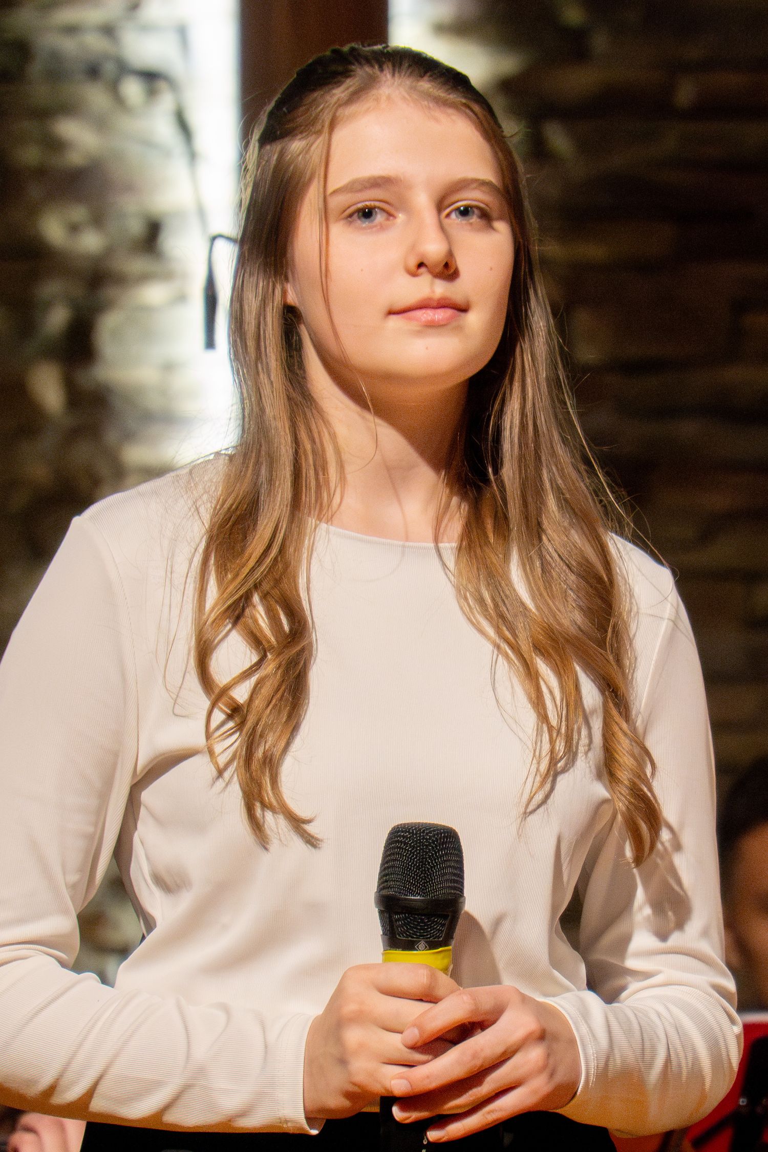 Young performer in white sweater holds microphone during church concert.