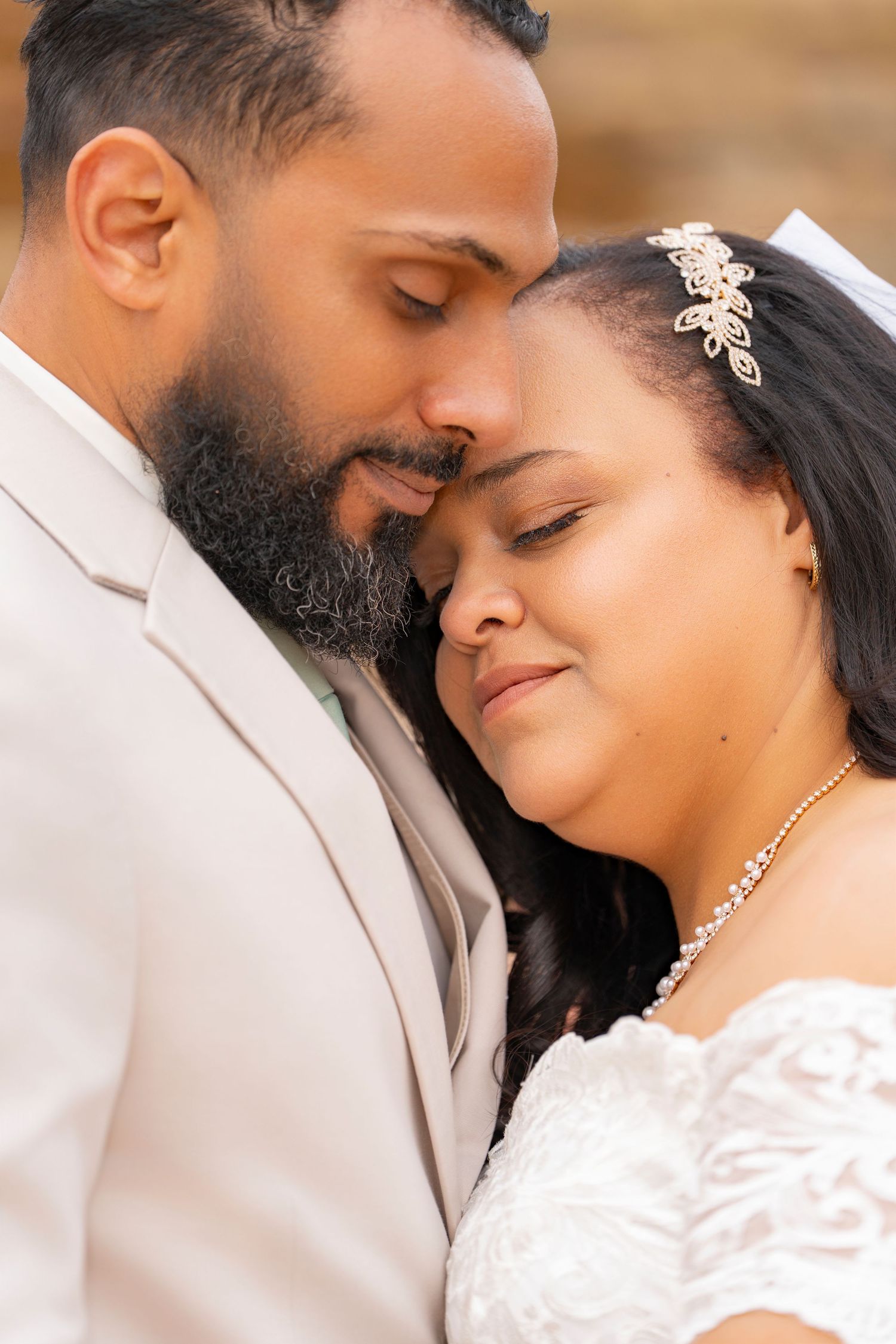 A tender wedding moment captured as newlyweds embrace, with the bride wearing a lace dress and crystal headpiece.