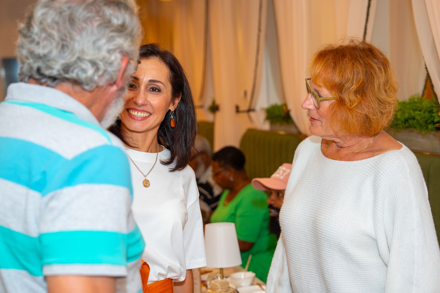 People socializing at tables in a brightly lit room with white decor.