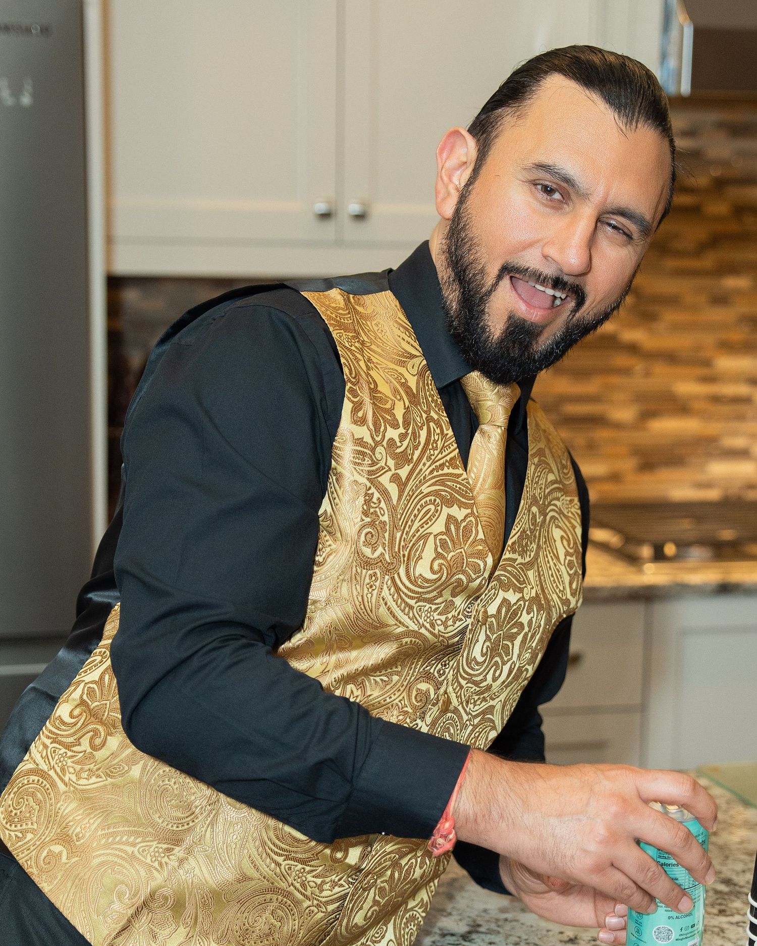 Person wearing a gold patterned vest and black shirt prepares food in a modern kitchen.