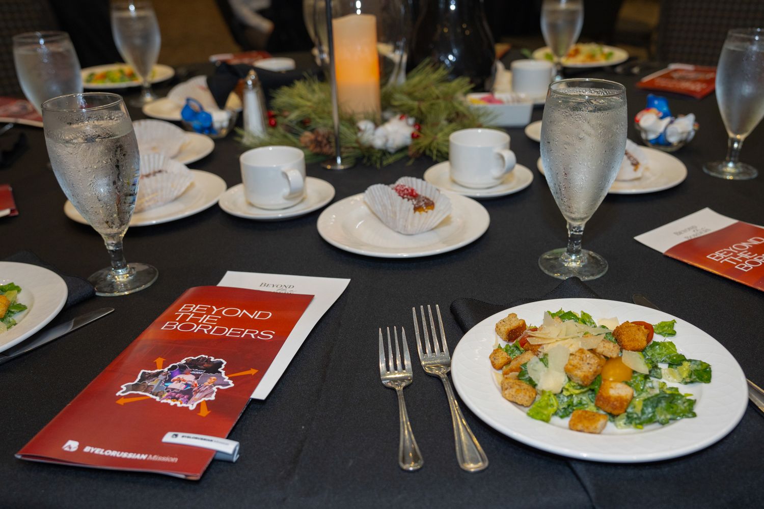 Place settings with plates, glasses and silverware arranged on round tables at a formal dinner.