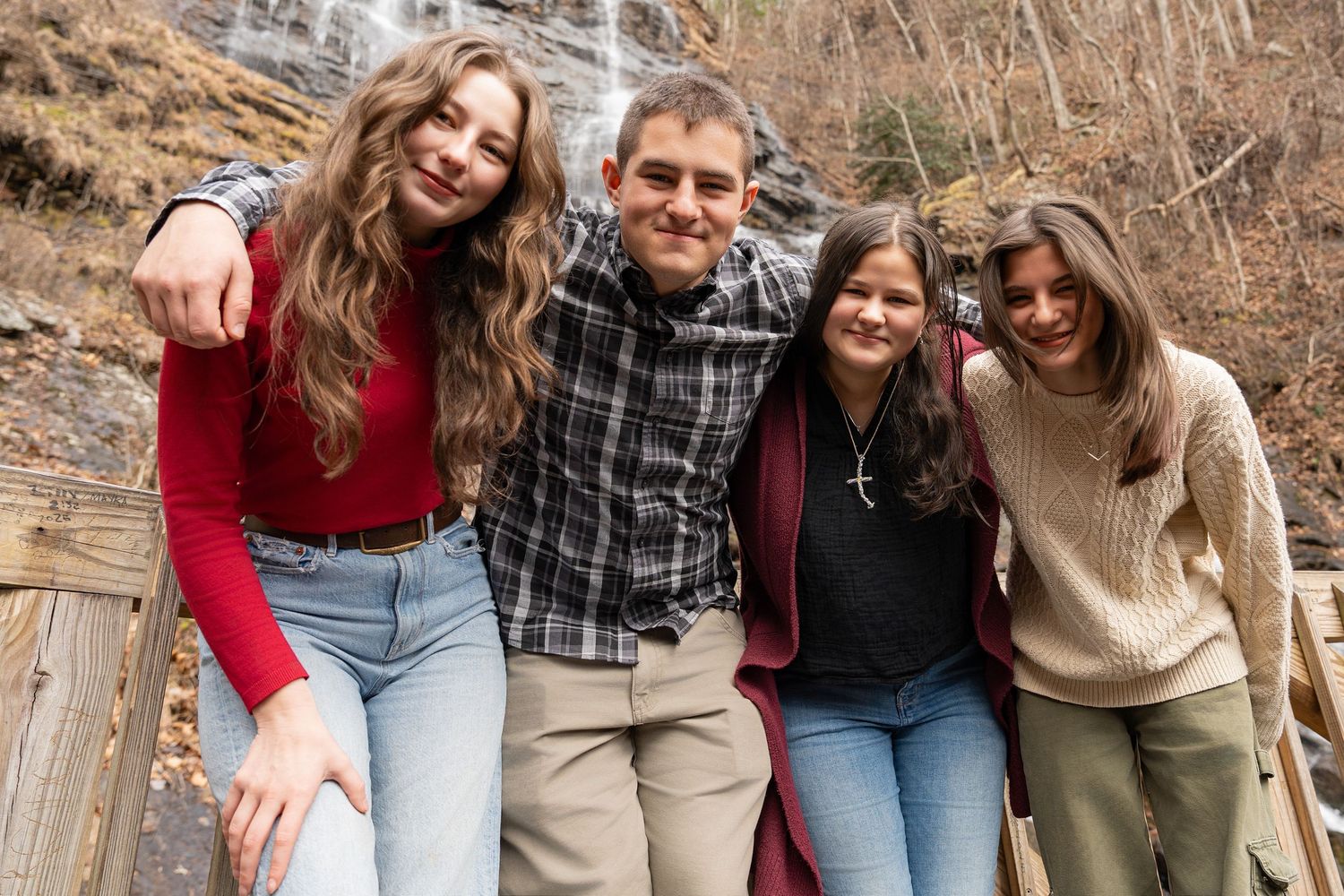 A group of friends laugh and smile together while posing outdoors on a winter day in casual attire.