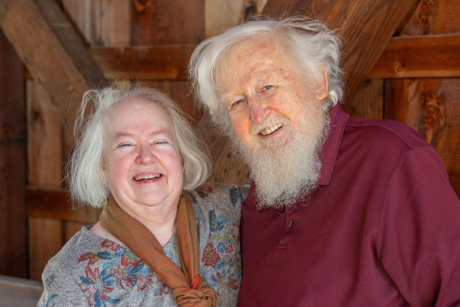 A joyful elderly couple laughs together while sitting in a rustic wooden interior.