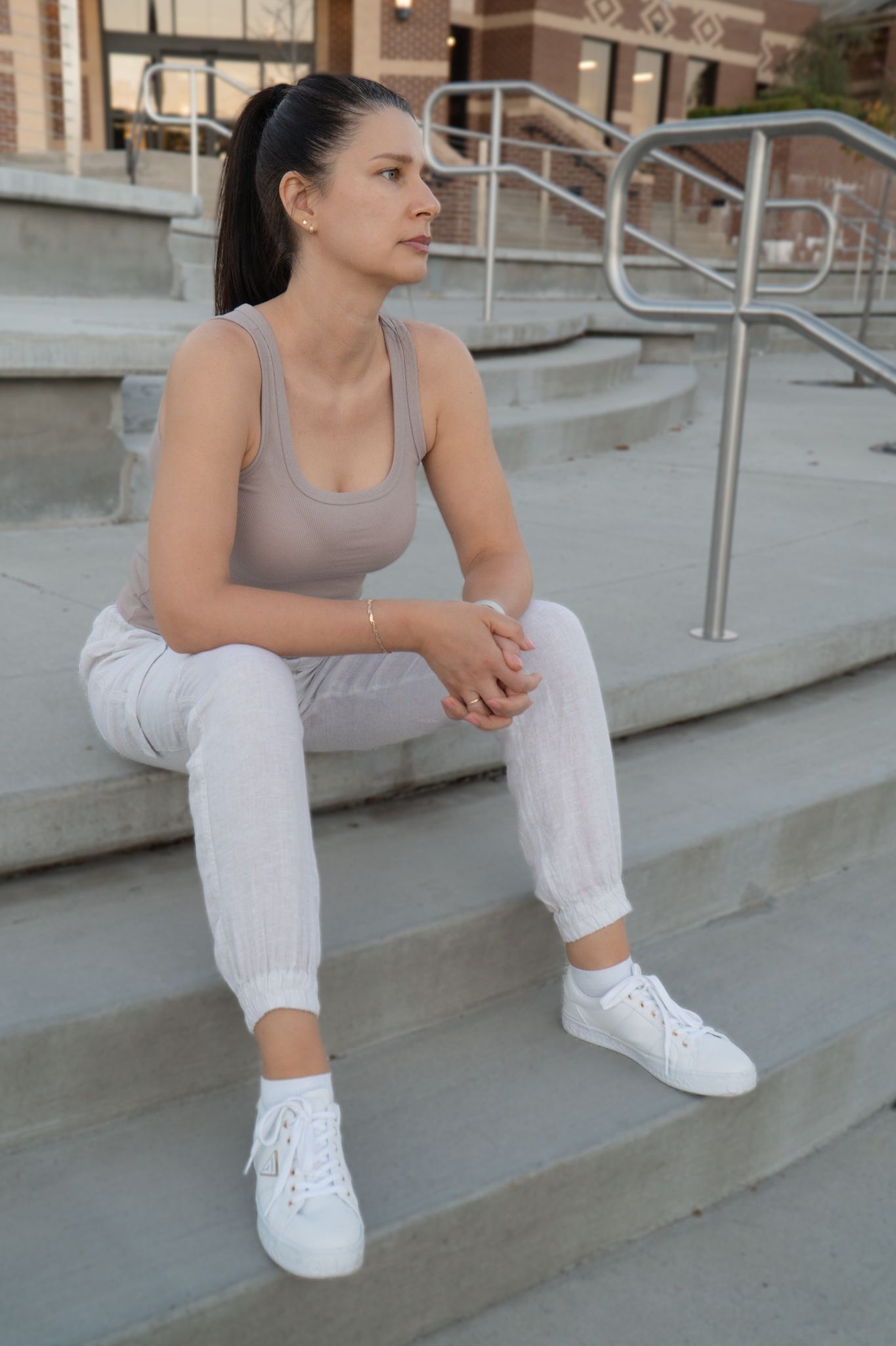 Figure in casual attire sitting on concrete steps wearing white sneakers.