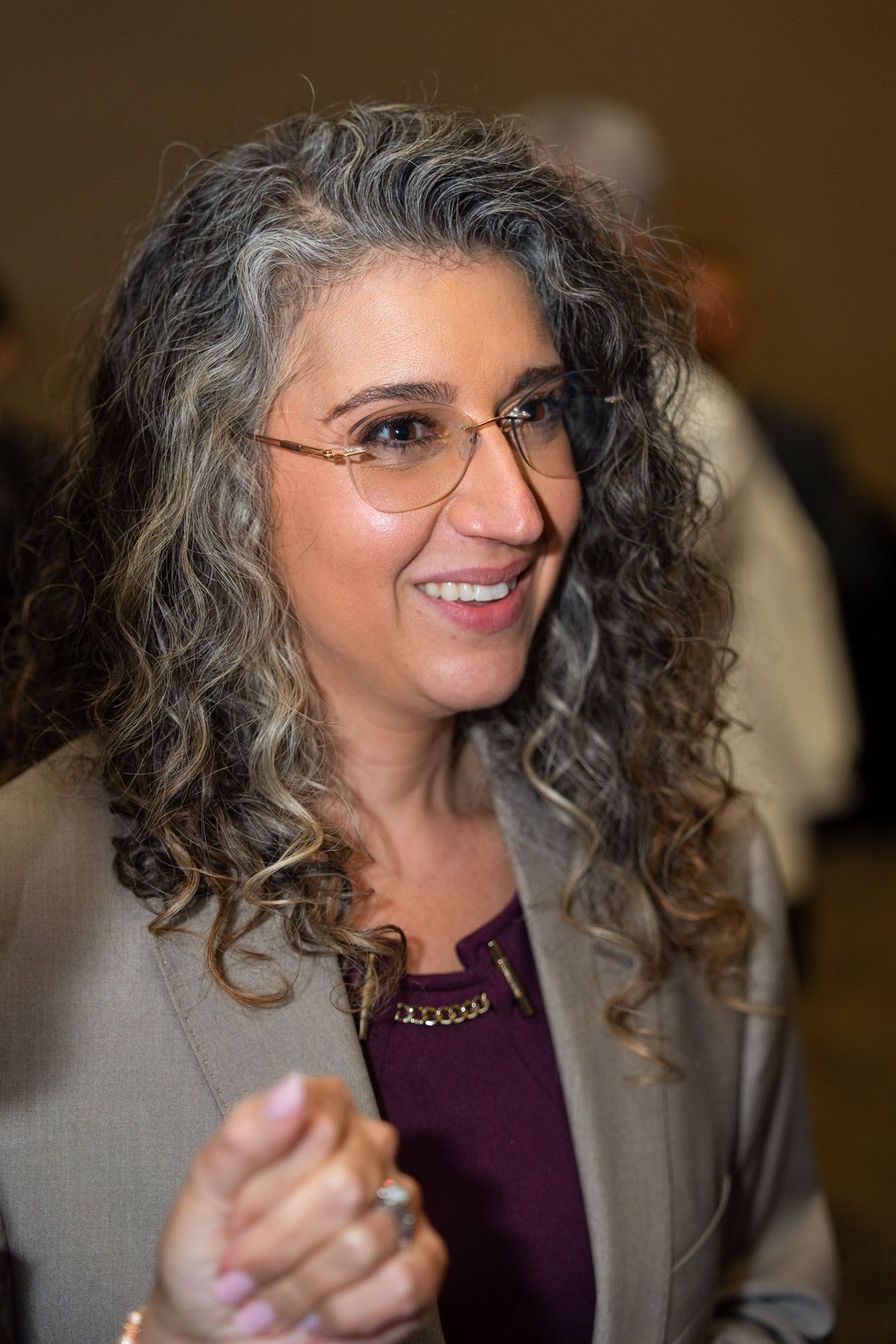 A professional wearing glasses and a gray blazer smiles warmly while engaged in conversation.
