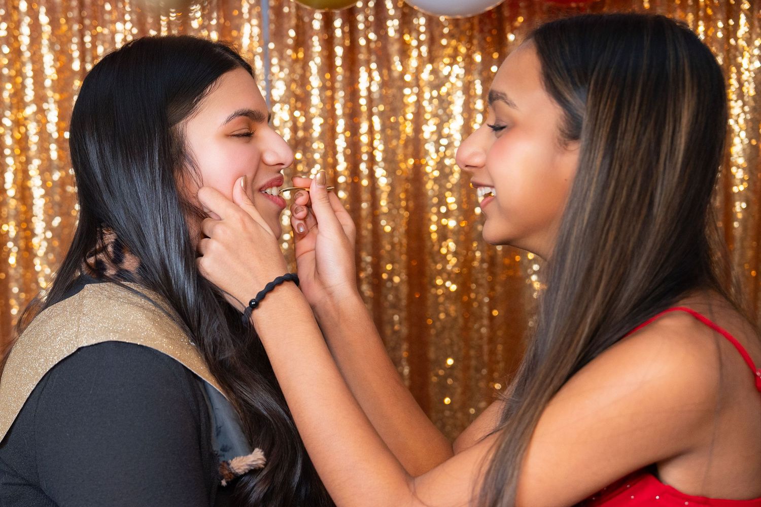Two people share a joyful moment together against a shimmering gold backdrop of hanging lights and decorations.