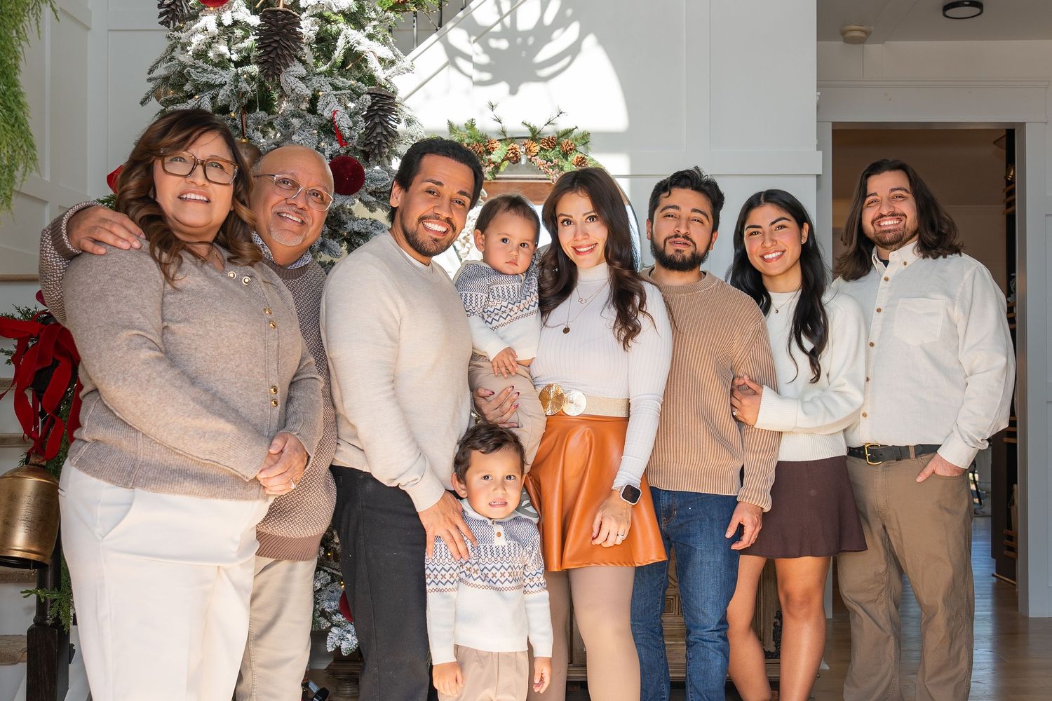 A large family gathering poses together in coordinated neutral outfits for a holiday photo shoot.
