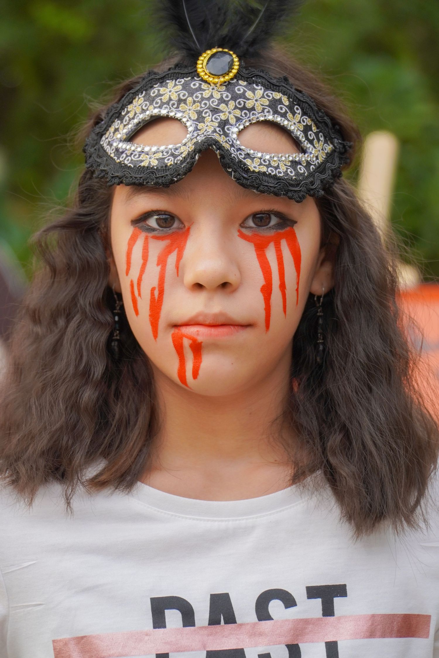 Creative Halloween makeup with red tears and metallic mask against natural background.