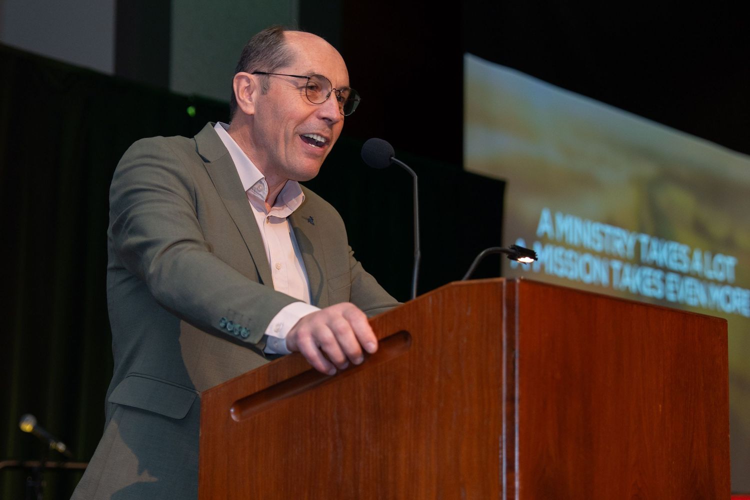A speaker stands at a podium delivering remarks during a presentation at an indoor event.