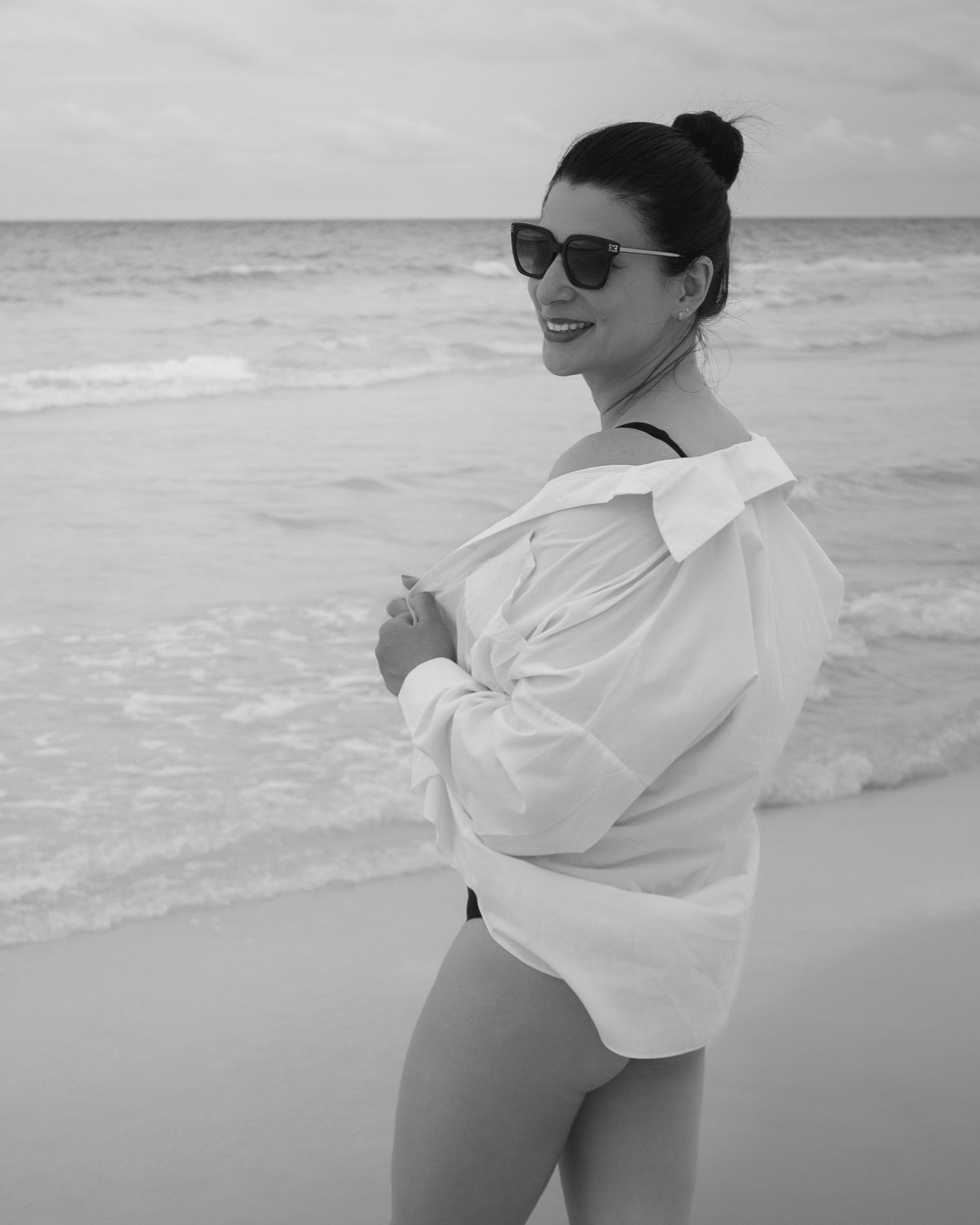 Person in white shirt poses on beach in black and white photograph.