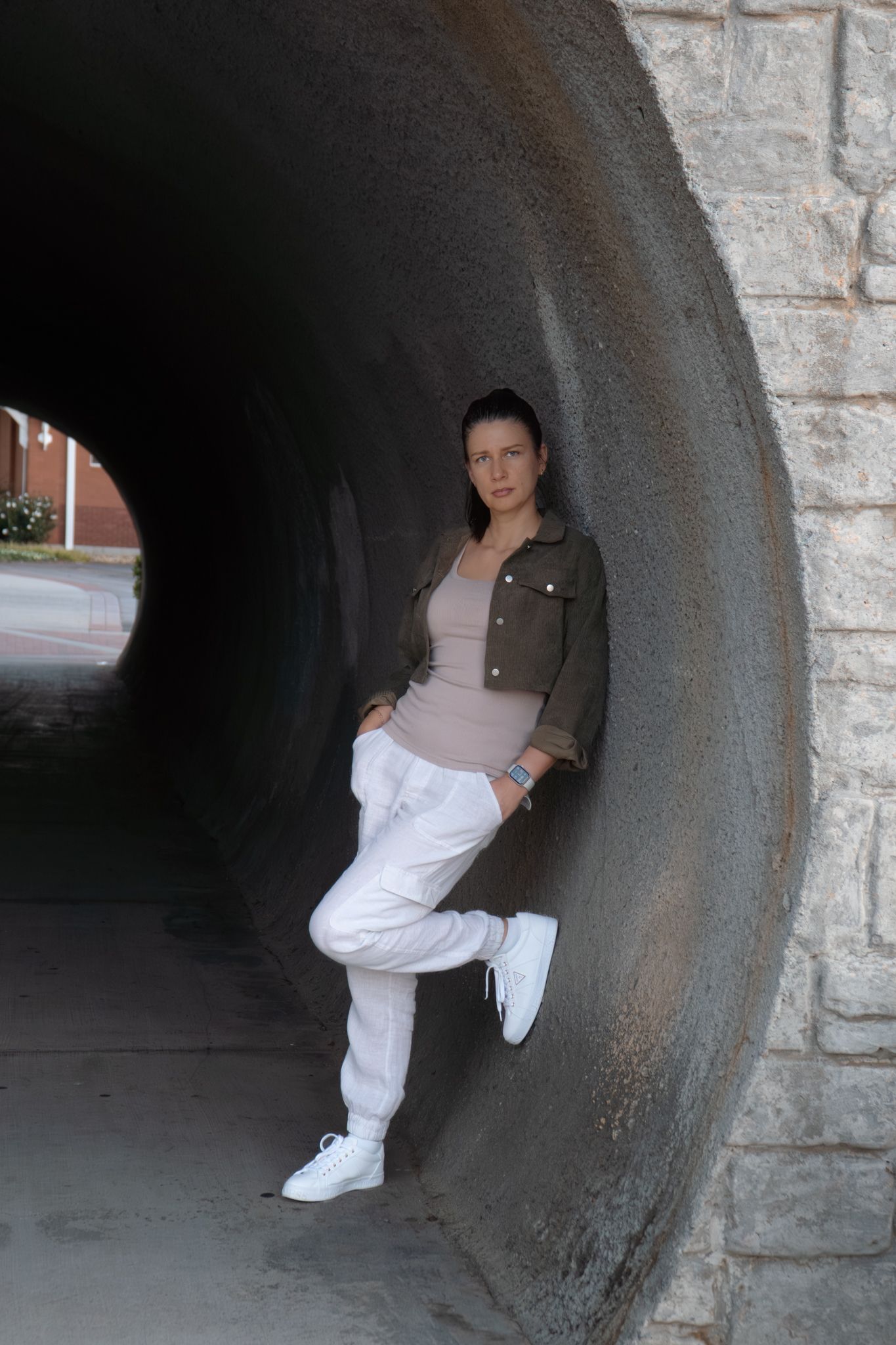 Figure in dark top and white pants posing inside concrete tunnel structure.