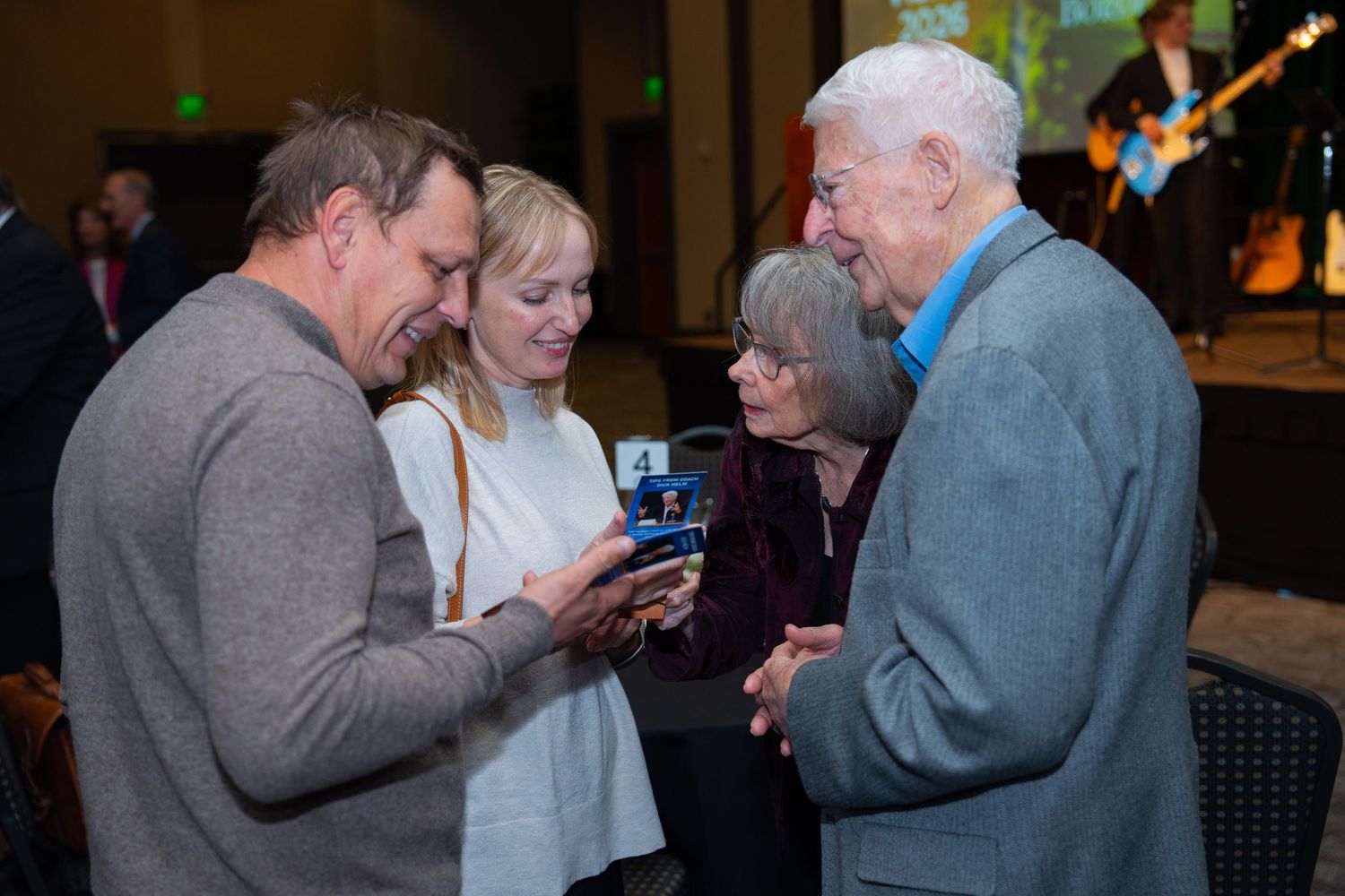 People in formal attire gathered at an event, looking at their mobile phones and digital devices.