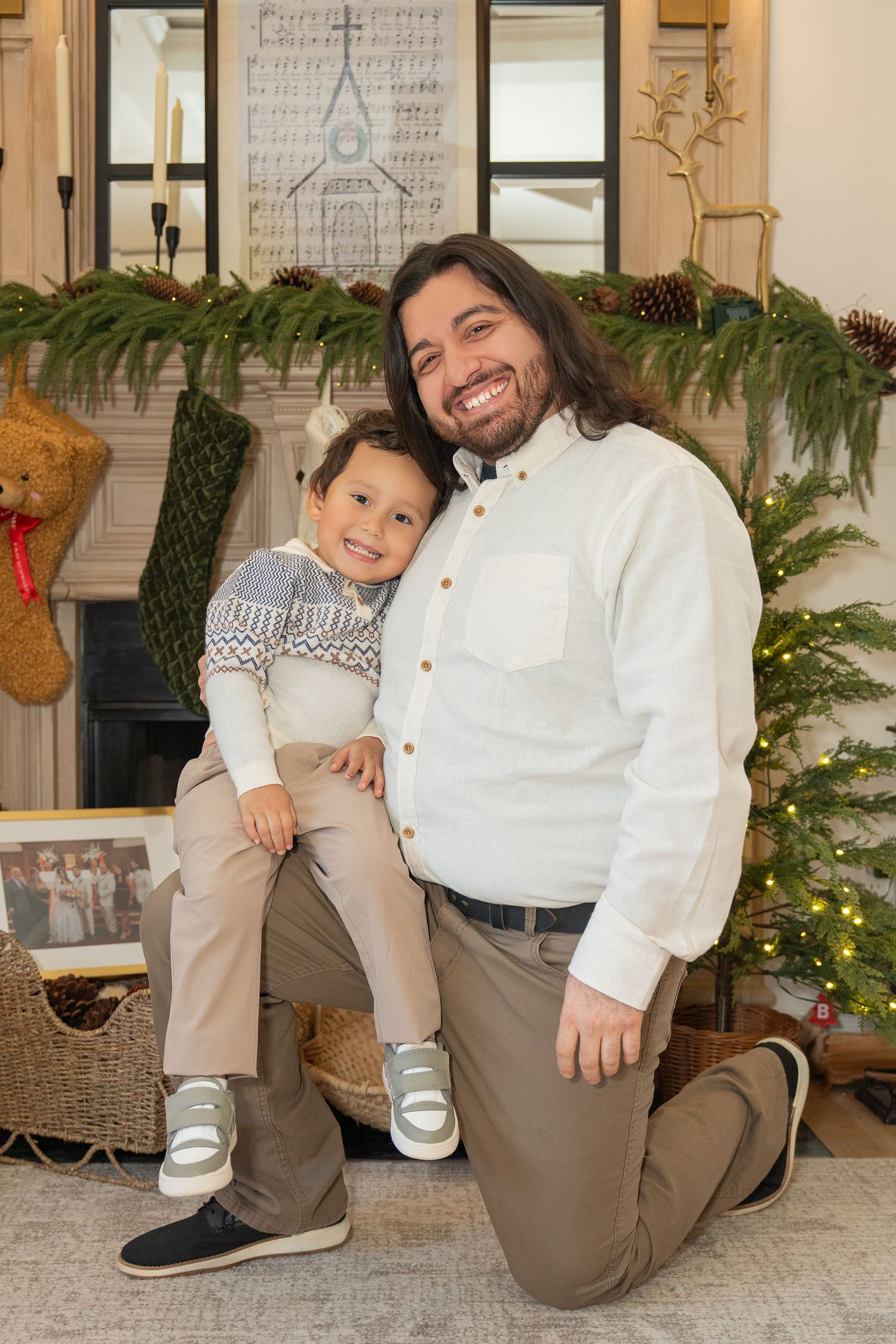 Holiday family portrait with people in matching white shirts and khaki pants posed near festive decorations.