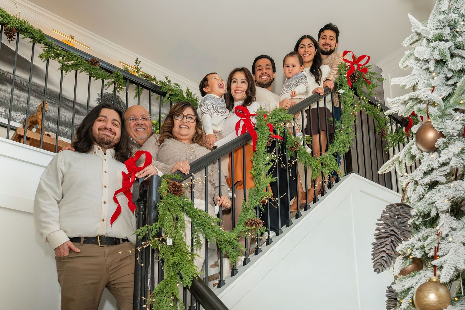 Wedding party members laugh joyfully while posing on a staircase decorated with holiday greenery and red bows.