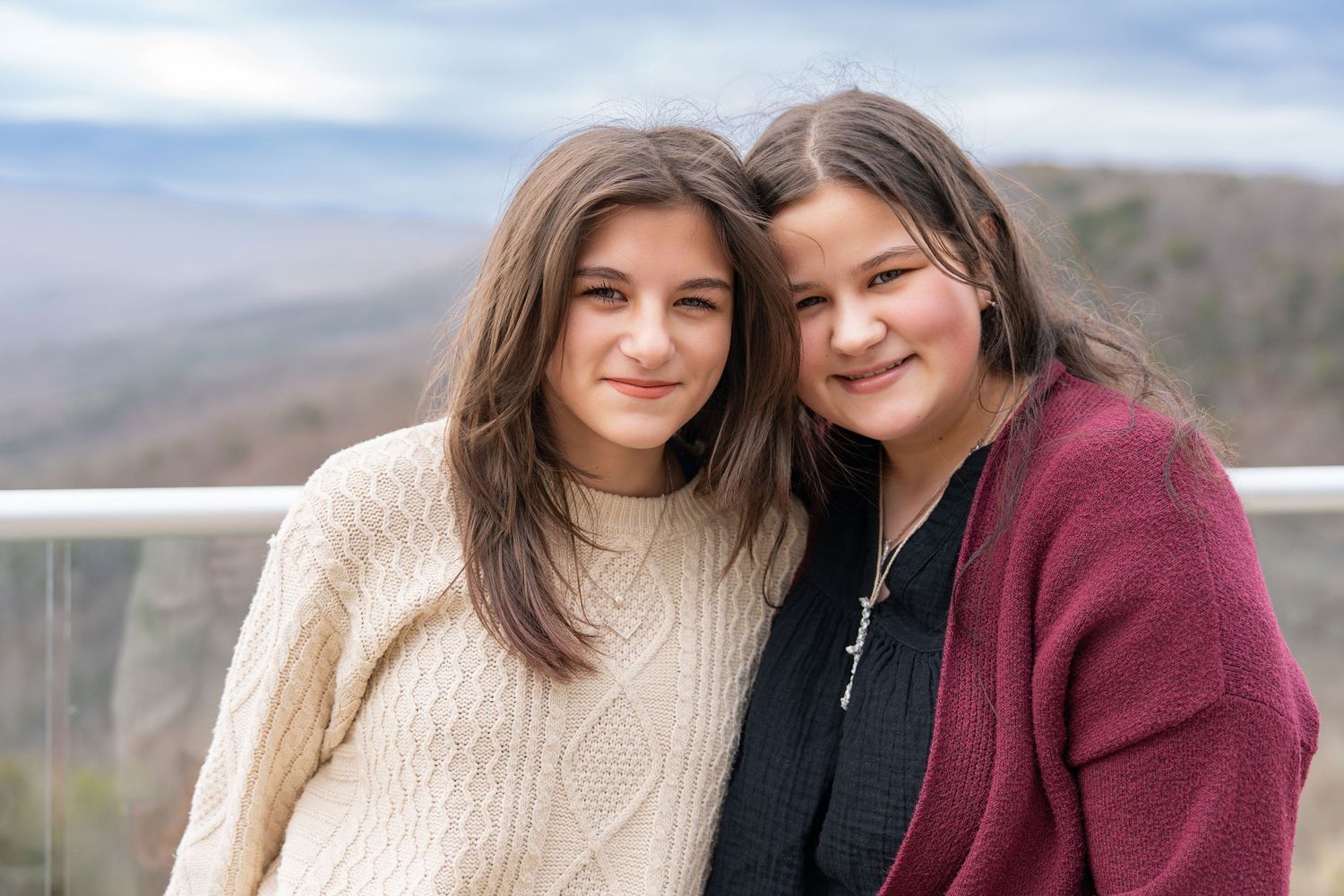 Two people in cozy sweaters embrace and smile while posing outdoors against a mountain backdrop.