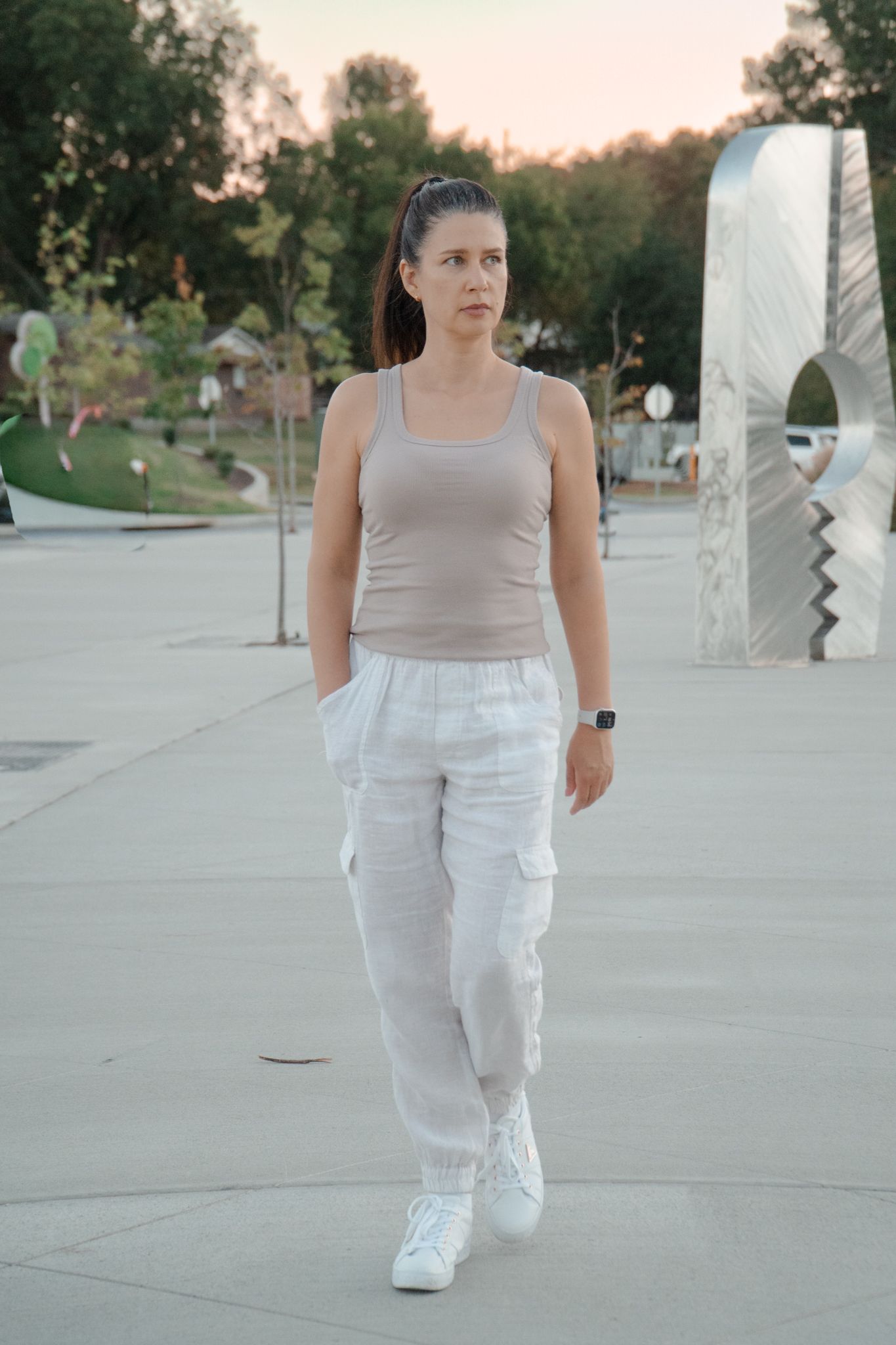 Person in neutral outfit walking on concrete path during sunset.