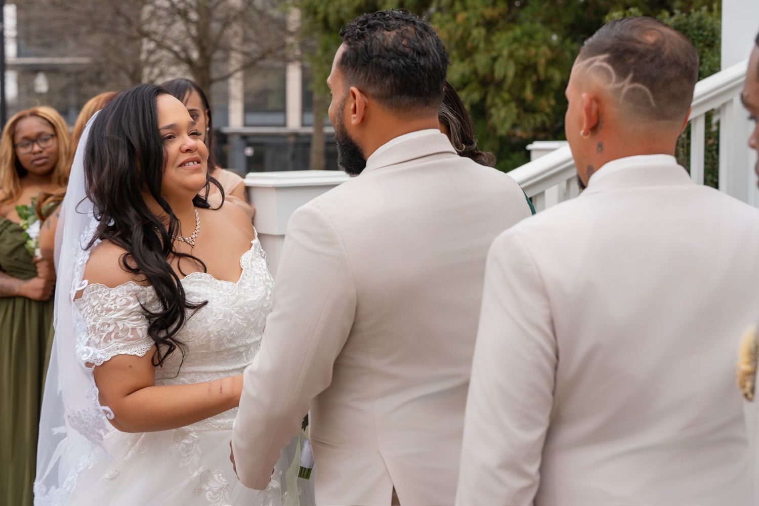 A joyful wedding ceremony moment with the couple and officiant wearing light beige and white attire outdoors.