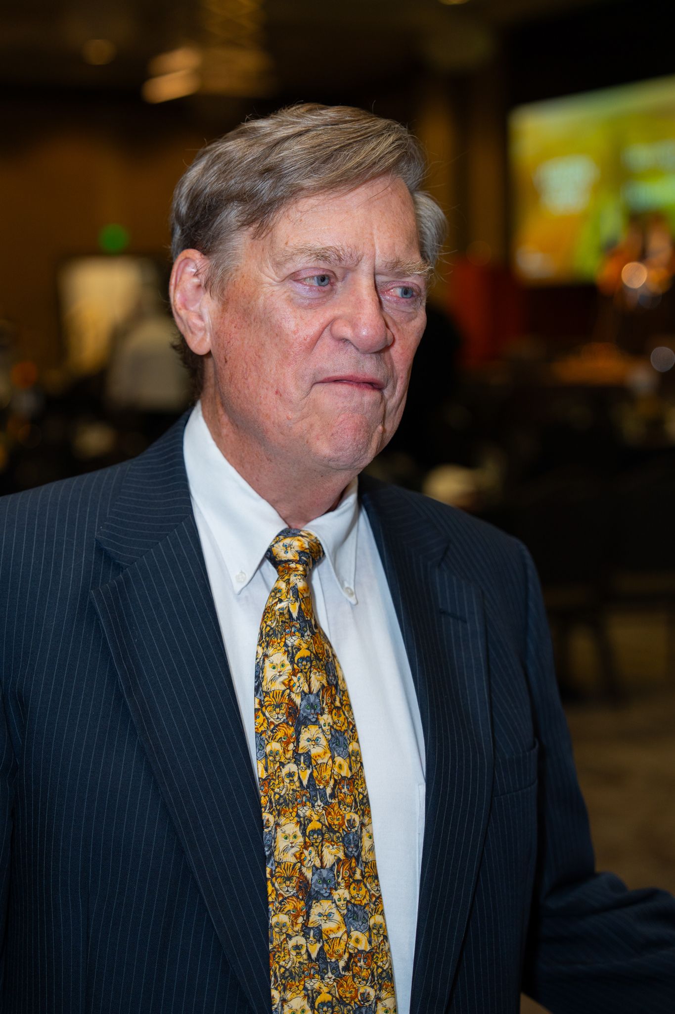 Person in pinstriped suit with patterned tie smiles at indoor event.