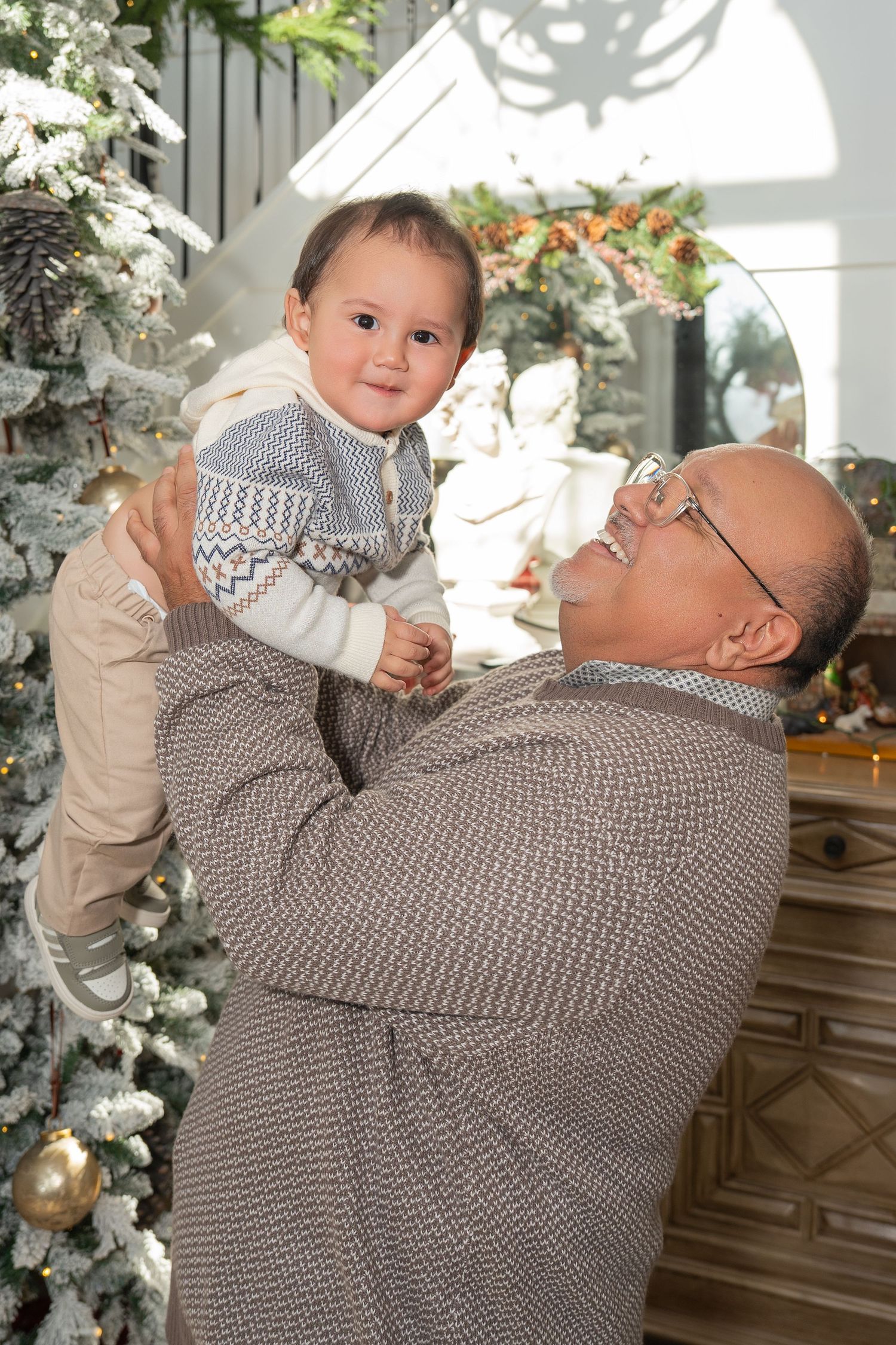 A heartwarming moment between an adult and baby during a Christmas photoshoot with decorated trees.