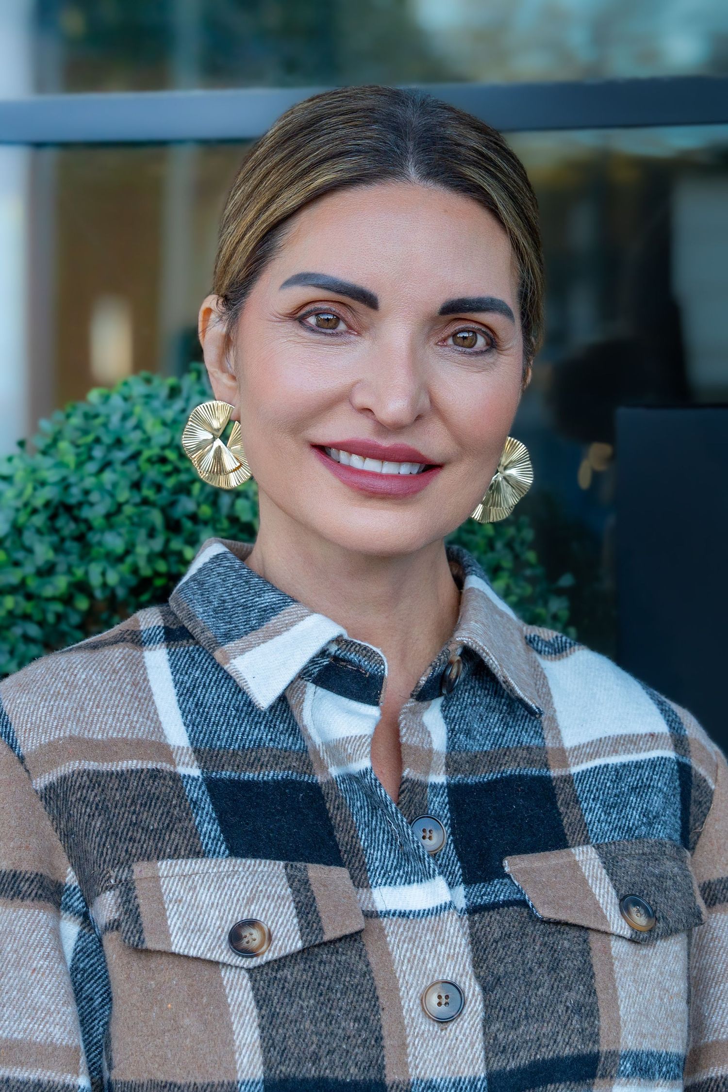 Fashionable person wearing a plaid shacket in brown and gray tones with gold statement earrings.