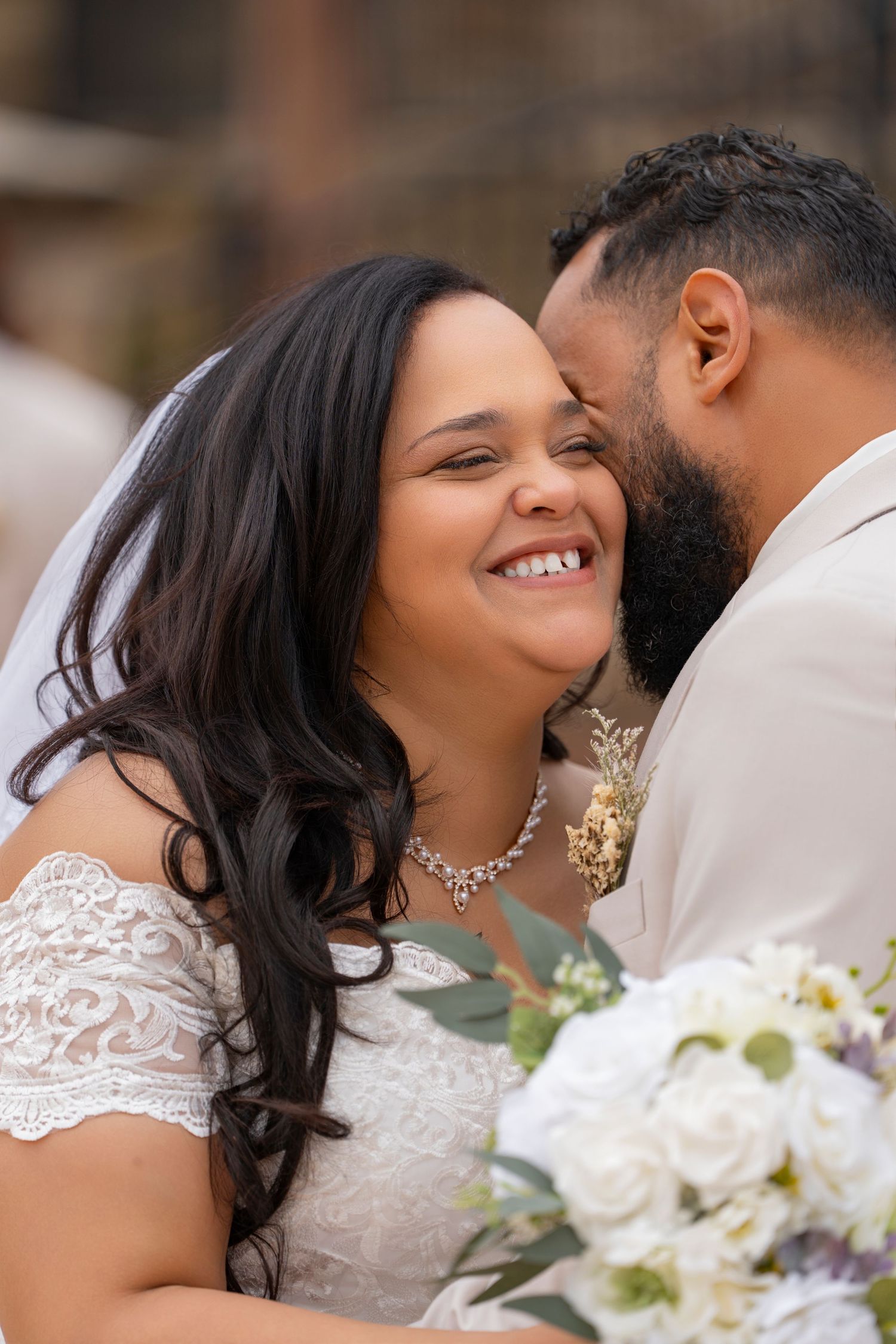 Romantic wedding couple sharing an intimate moment with white floral bouquet and lace dress details.