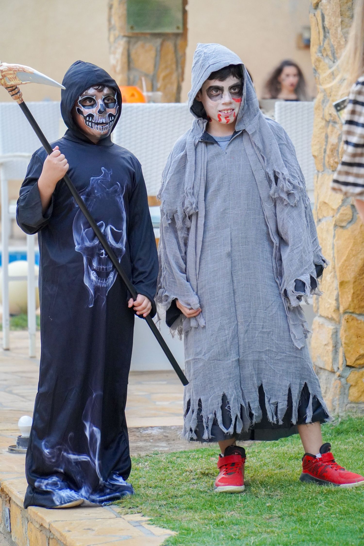 Children in ghost costumes with tattered gray robes playing outdoors.