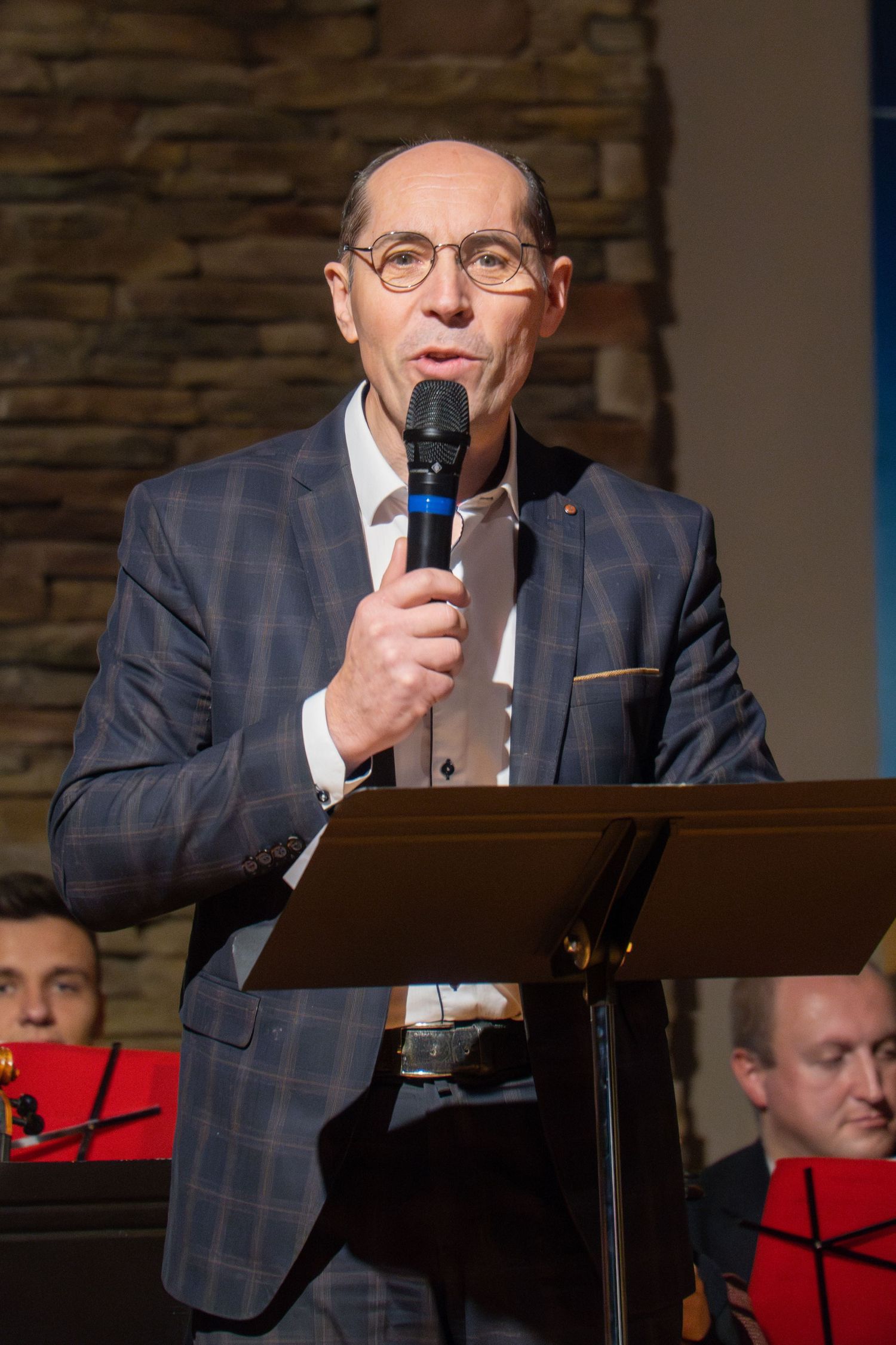 Speaker at podium delivers message during church concert event.
