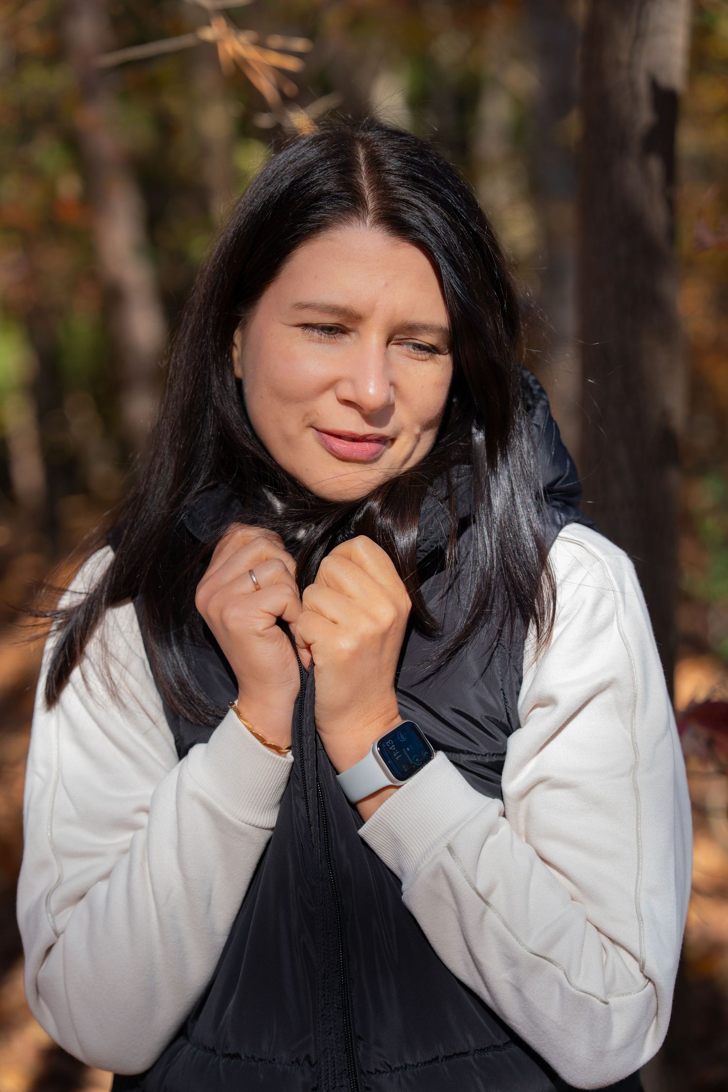 Person in white sweater and black vest poses outdoors during autumn.
