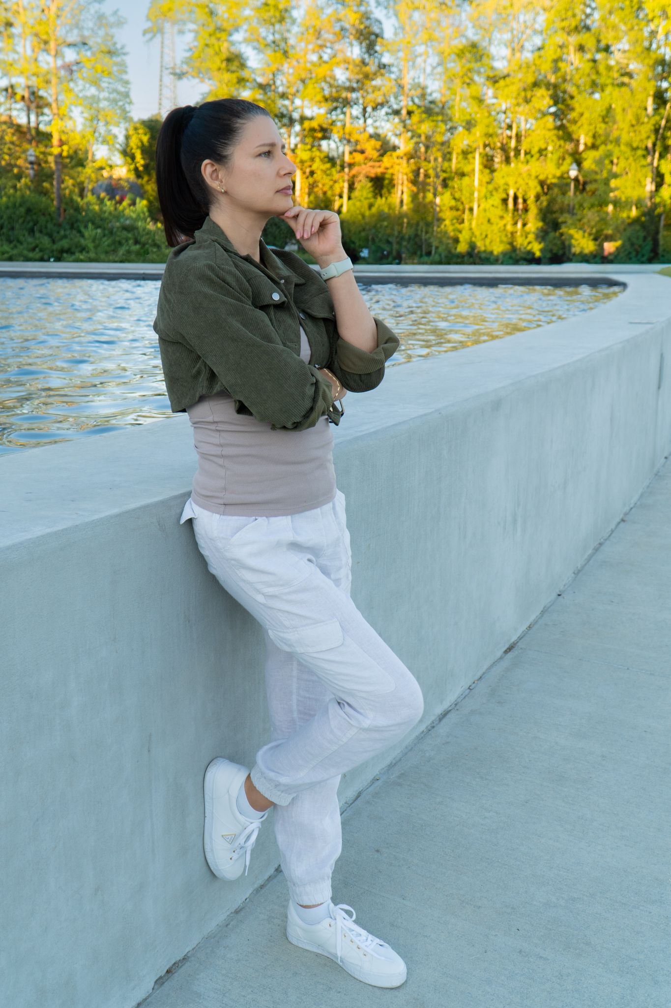 Figure in casual attire posing against concrete wall with autumn foliage in background.