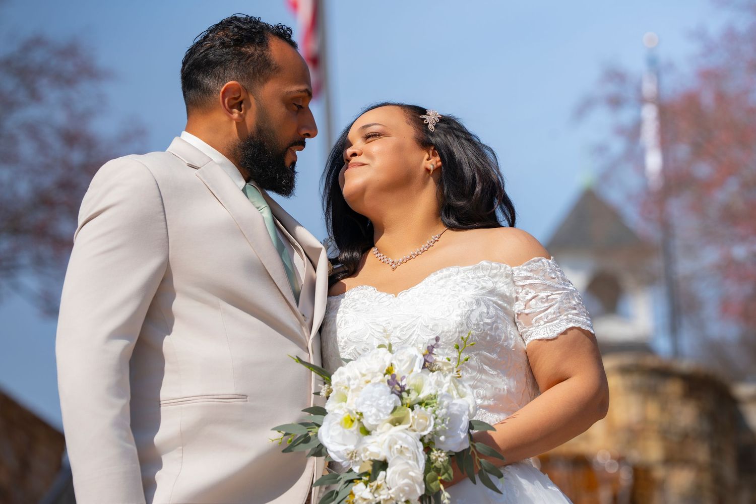 A happy couple shares a tender moment on their wedding day, with the bride holding a white floral bouquet.