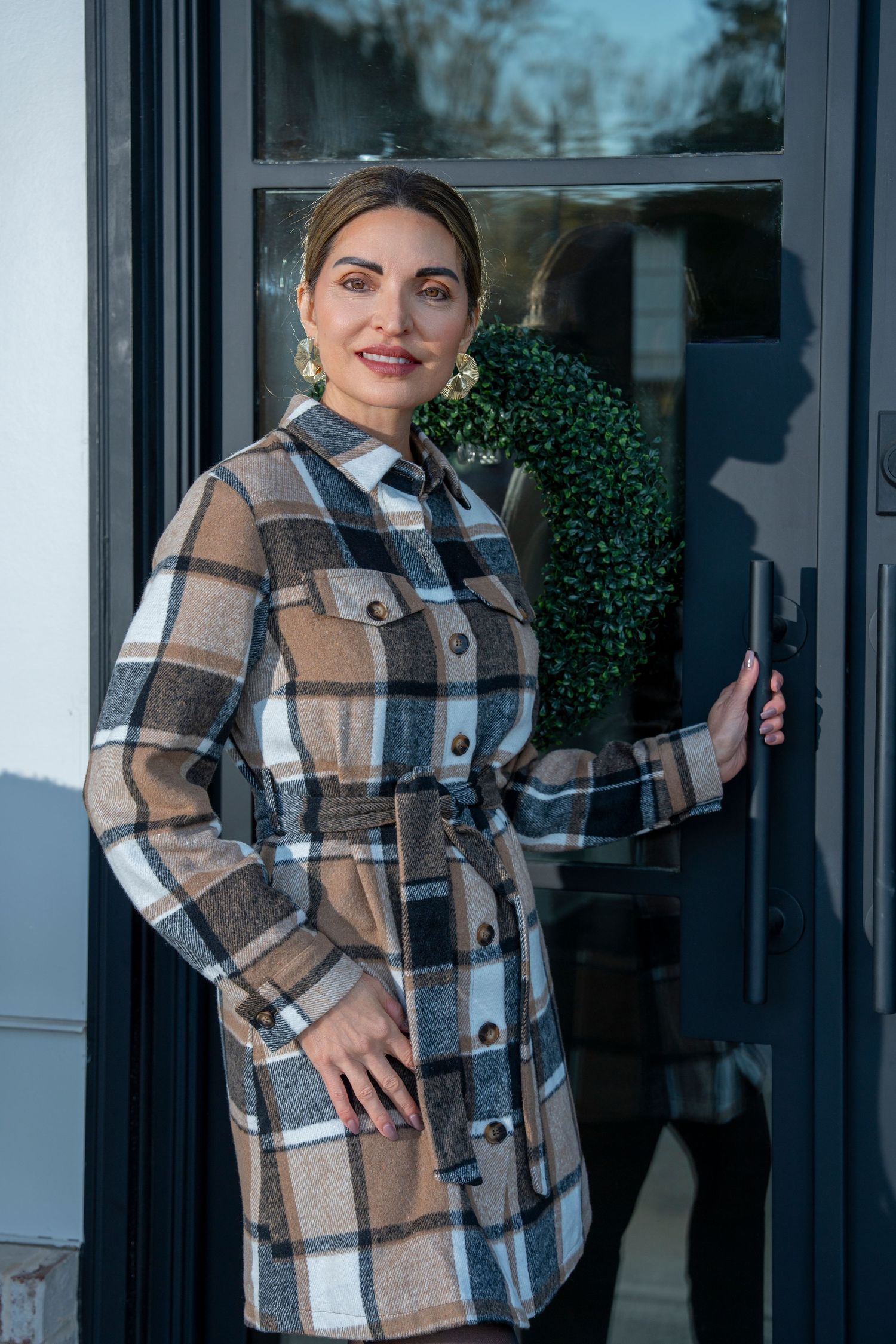 A cozy plaid shacket in brown and white tones is modeled in three different poses against a dark doorway.