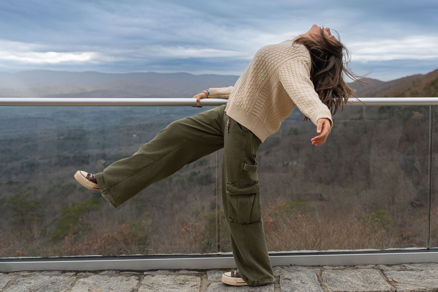 A person stands on a mountain overlook railing, creating a sequence of playful poses against a scenic vista background.