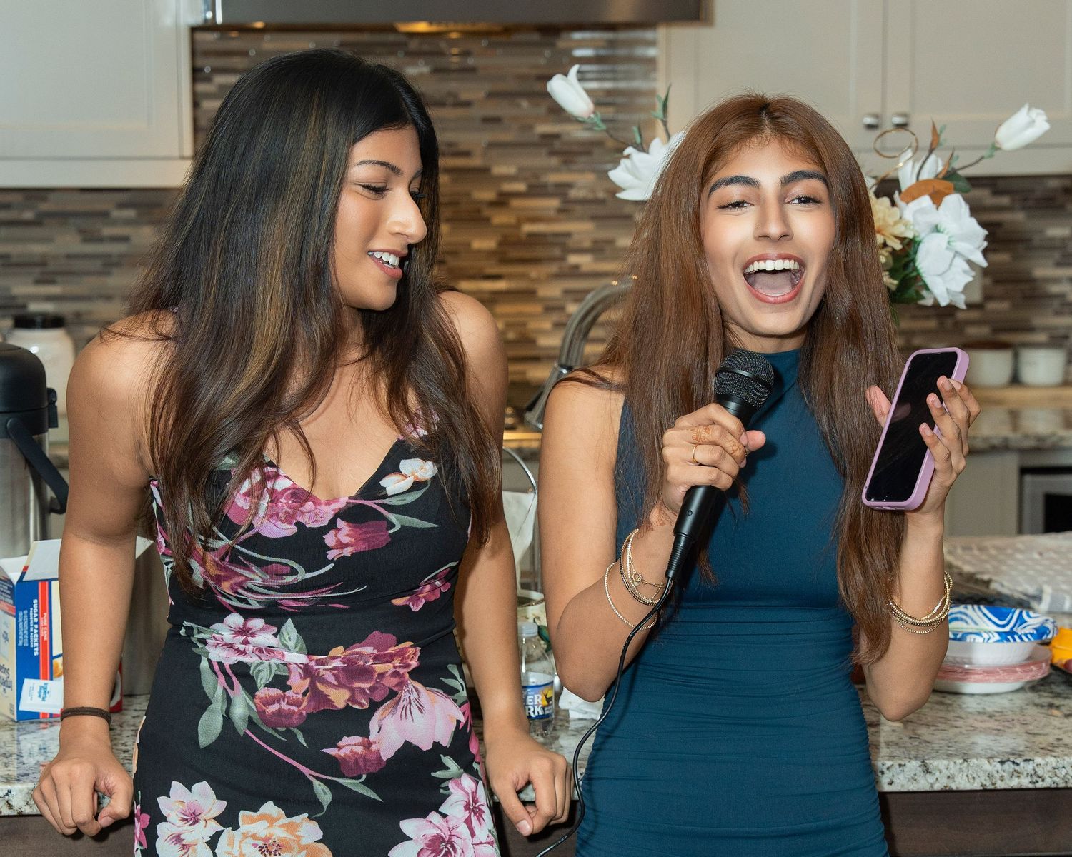 A group of friends laugh and smile together while gathered around a kitchen counter during a social gathering.