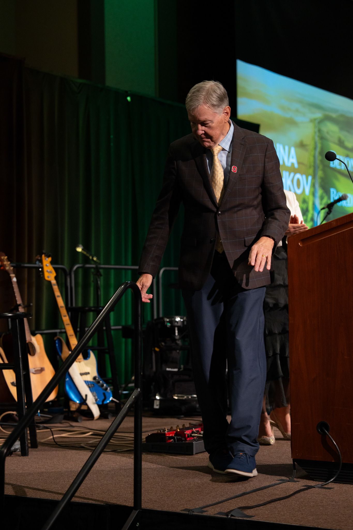 A presenter walks across a darkened stage during a conference presentation.