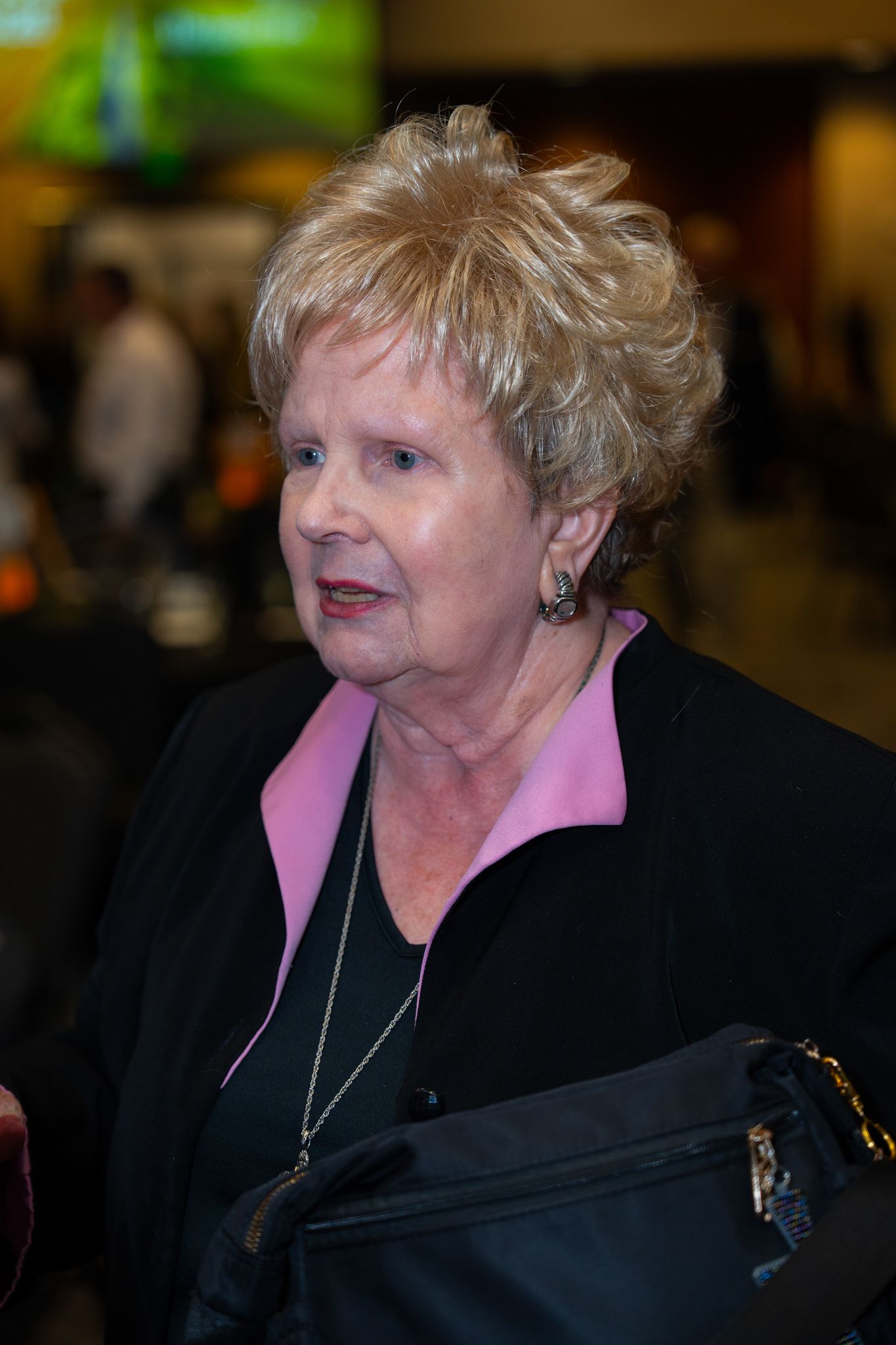 Person wearing black jacket and pink blouse at indoor gathering.