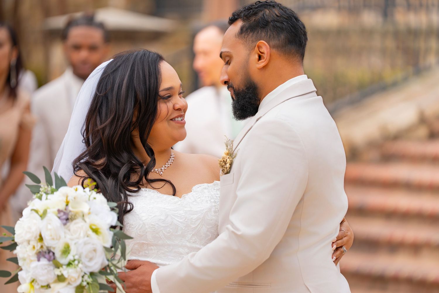 A couple shares an intimate moment during their wedding photoshoot on stone steps with white floral bouquet details.