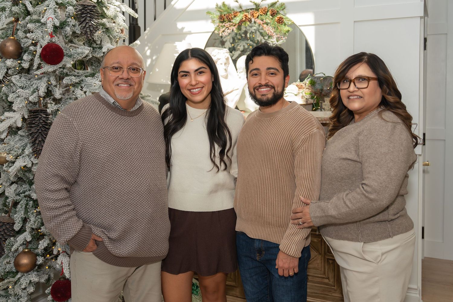 A group of people wearing coordinated beige and brown sweaters pose together in front of a decorated Christmas tree.