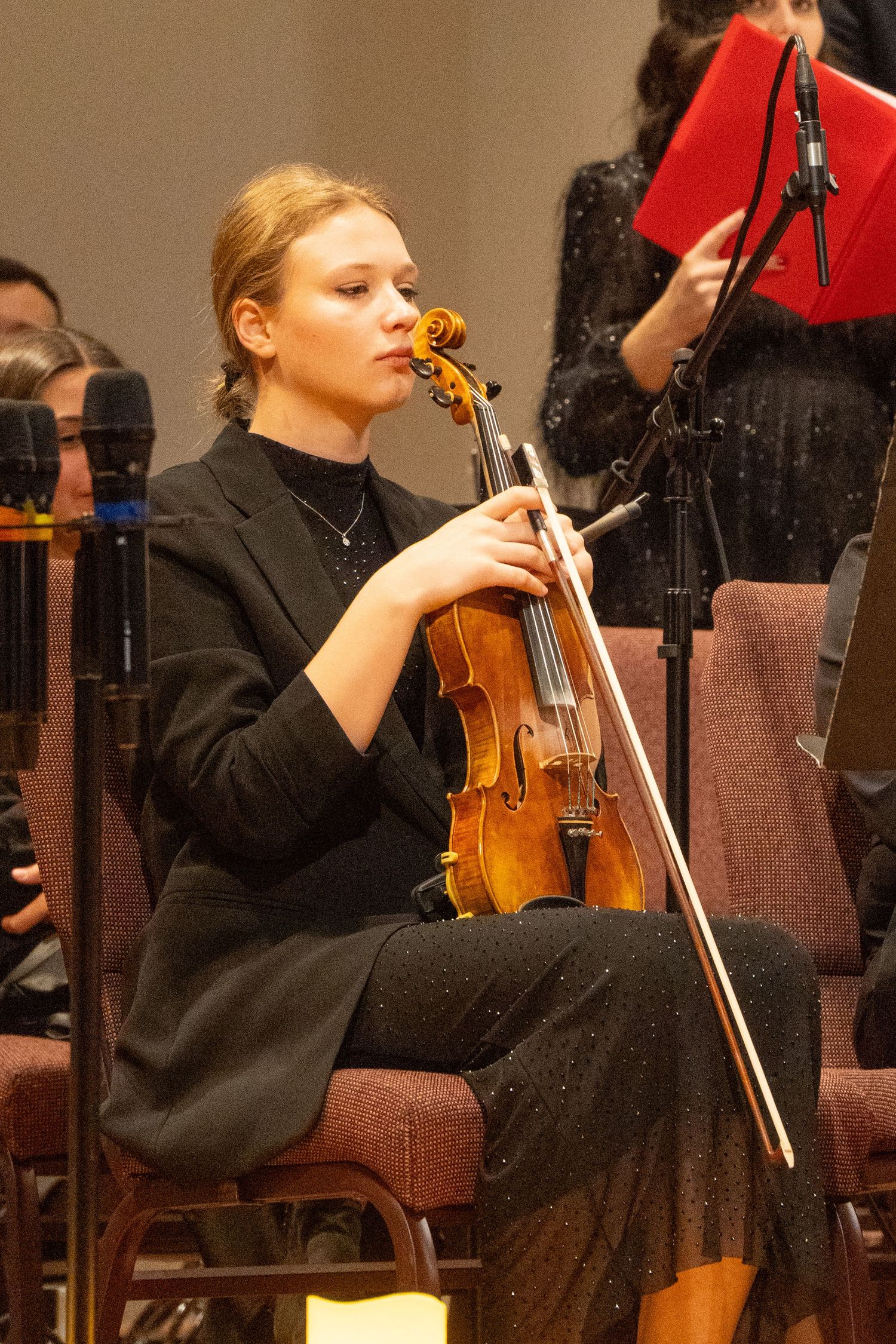 Violinist in black attire performs during concert with orchestra.