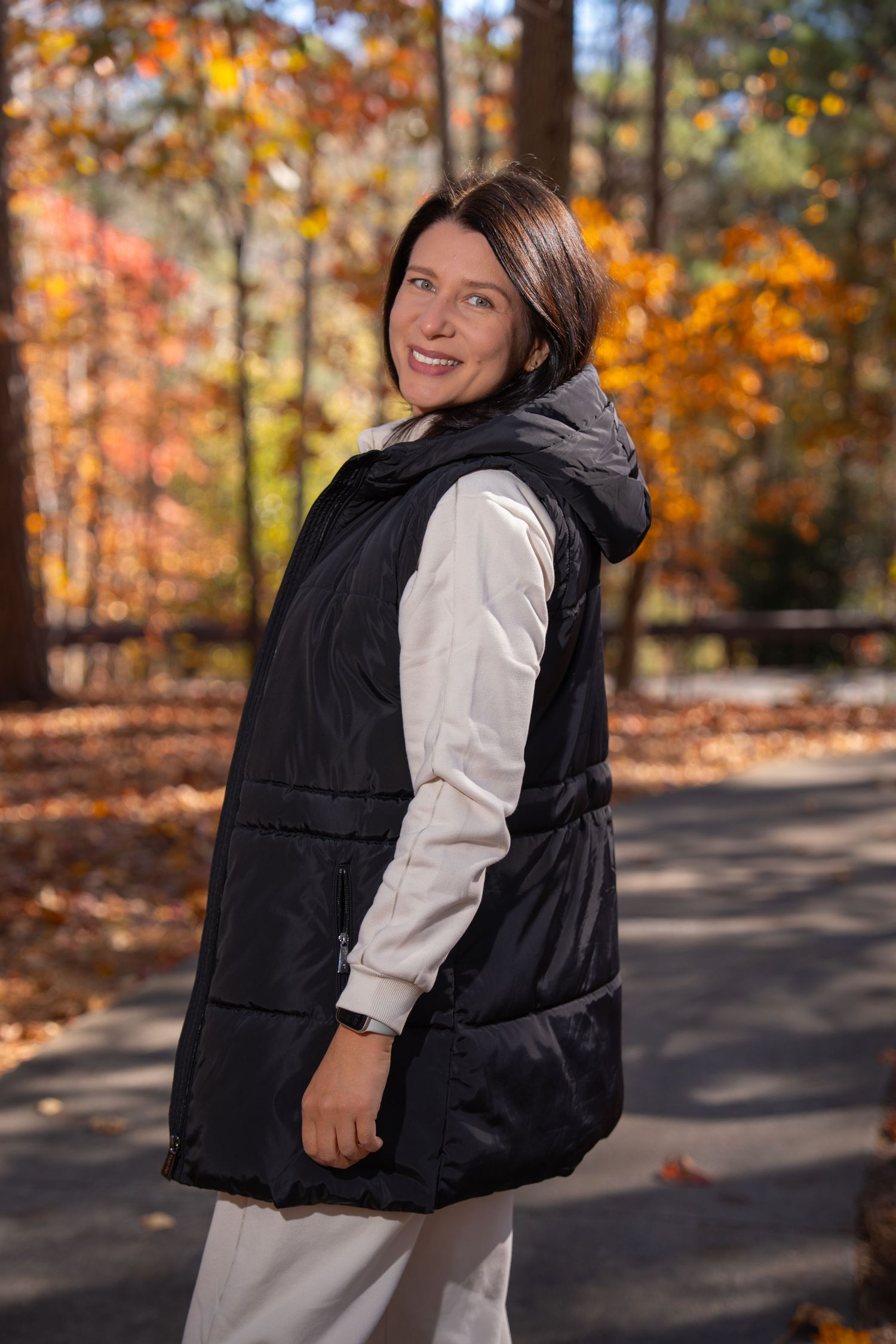 Person in casual attire poses playfully on forest path during fall season.