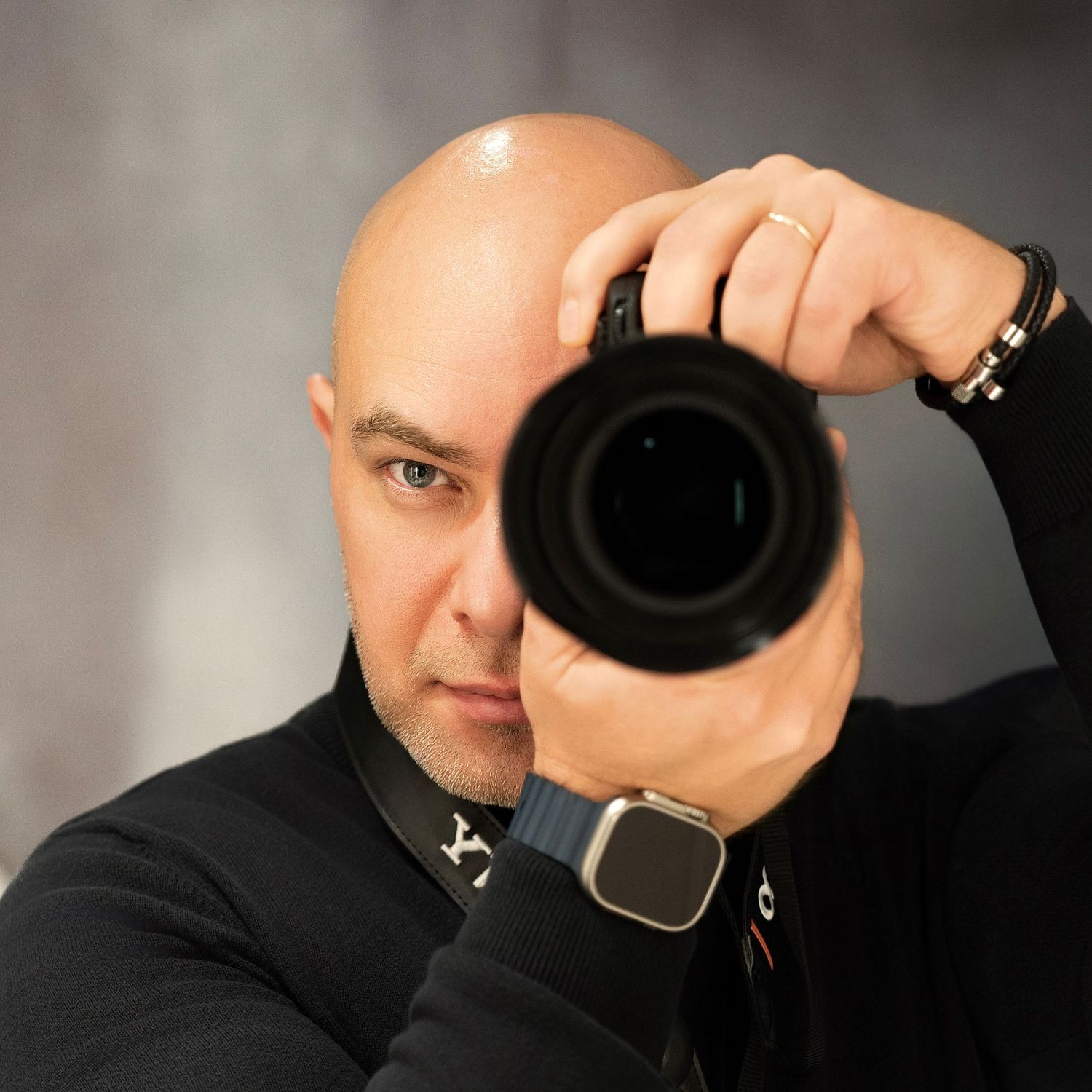 Professional photographer wearing black clothing holds a camera up to their eye while taking a photograph.