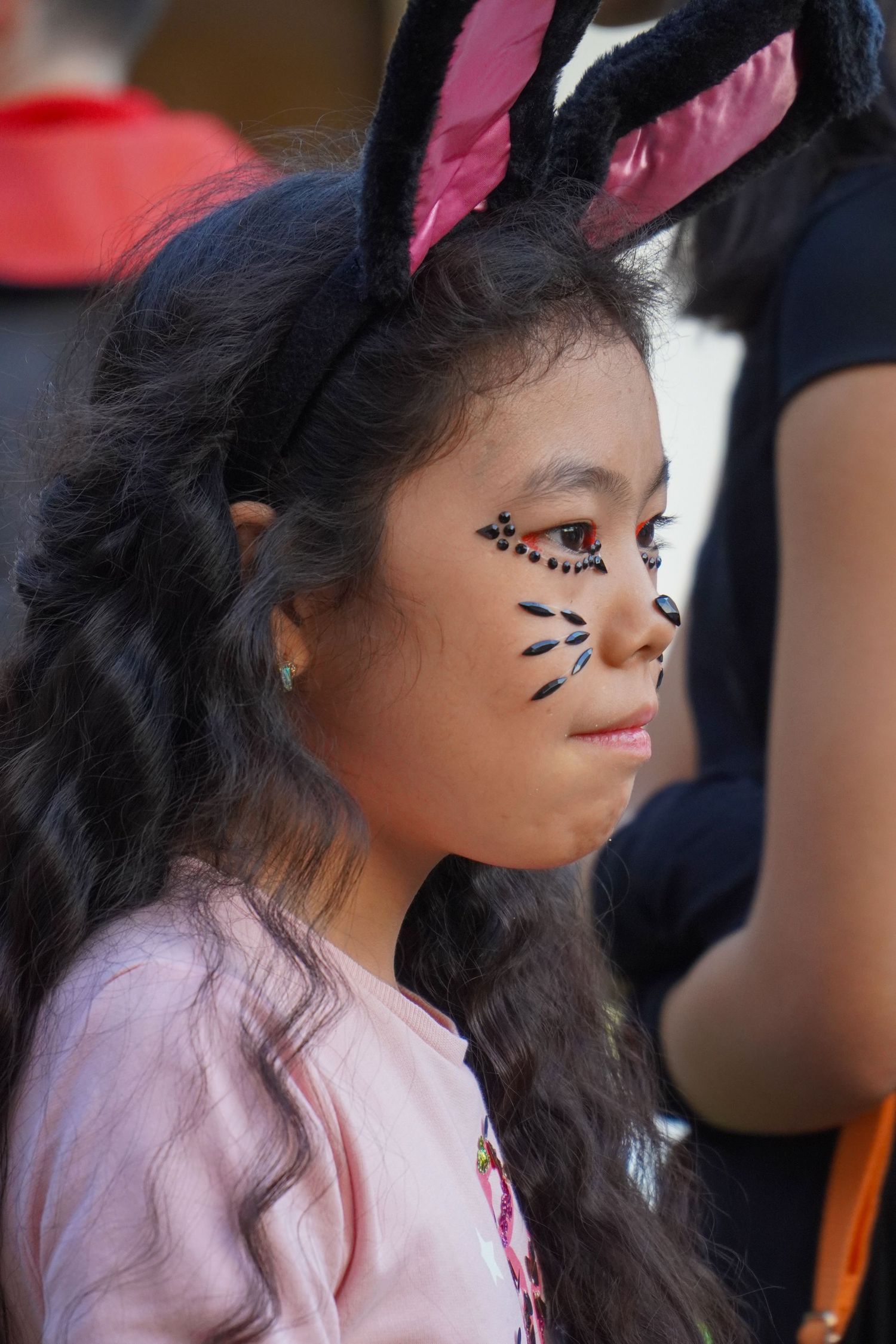 Halloween face paint design featuring delicate black dots and pink accessories.