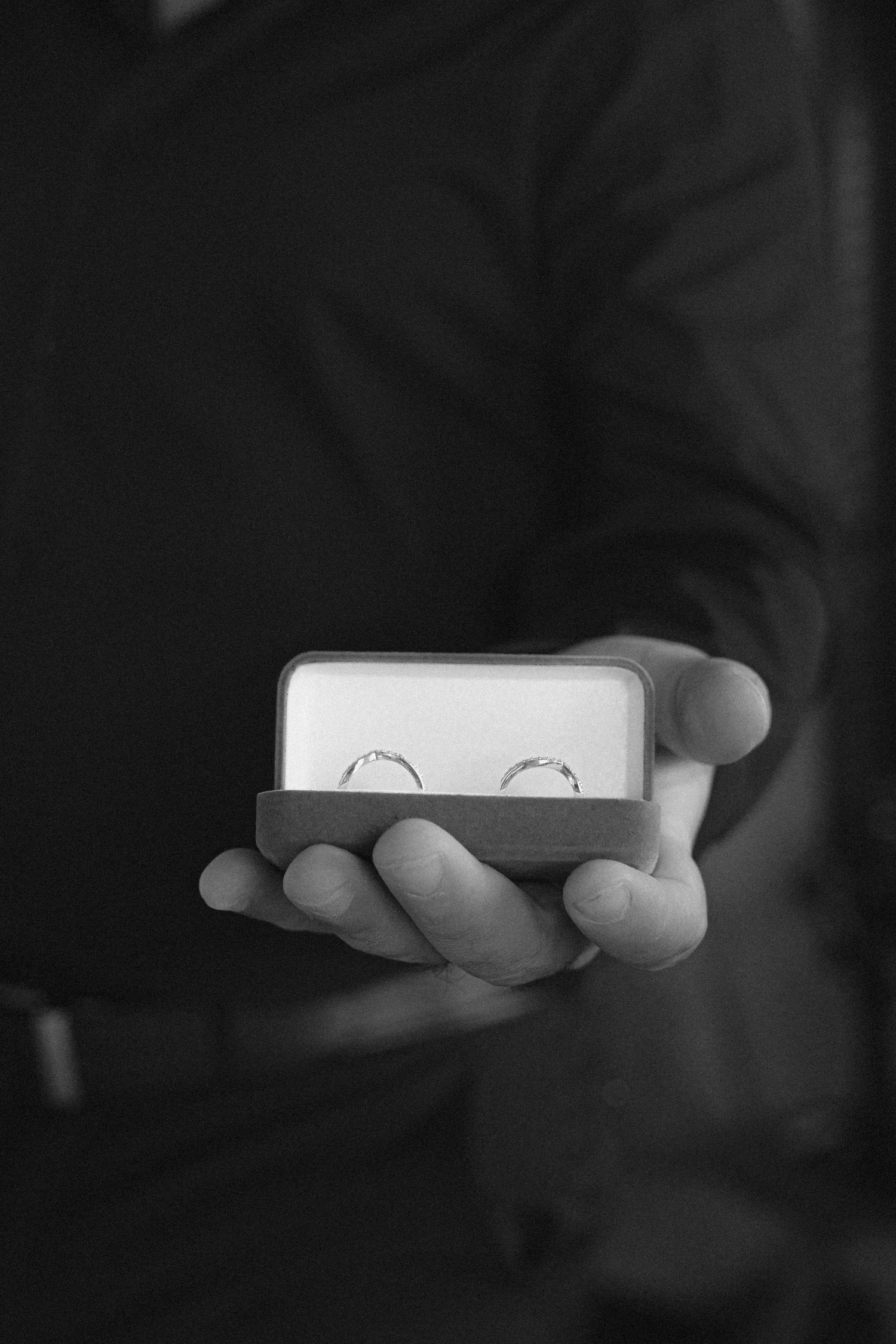 Black and white image of hands holding a small white box against a dark background.