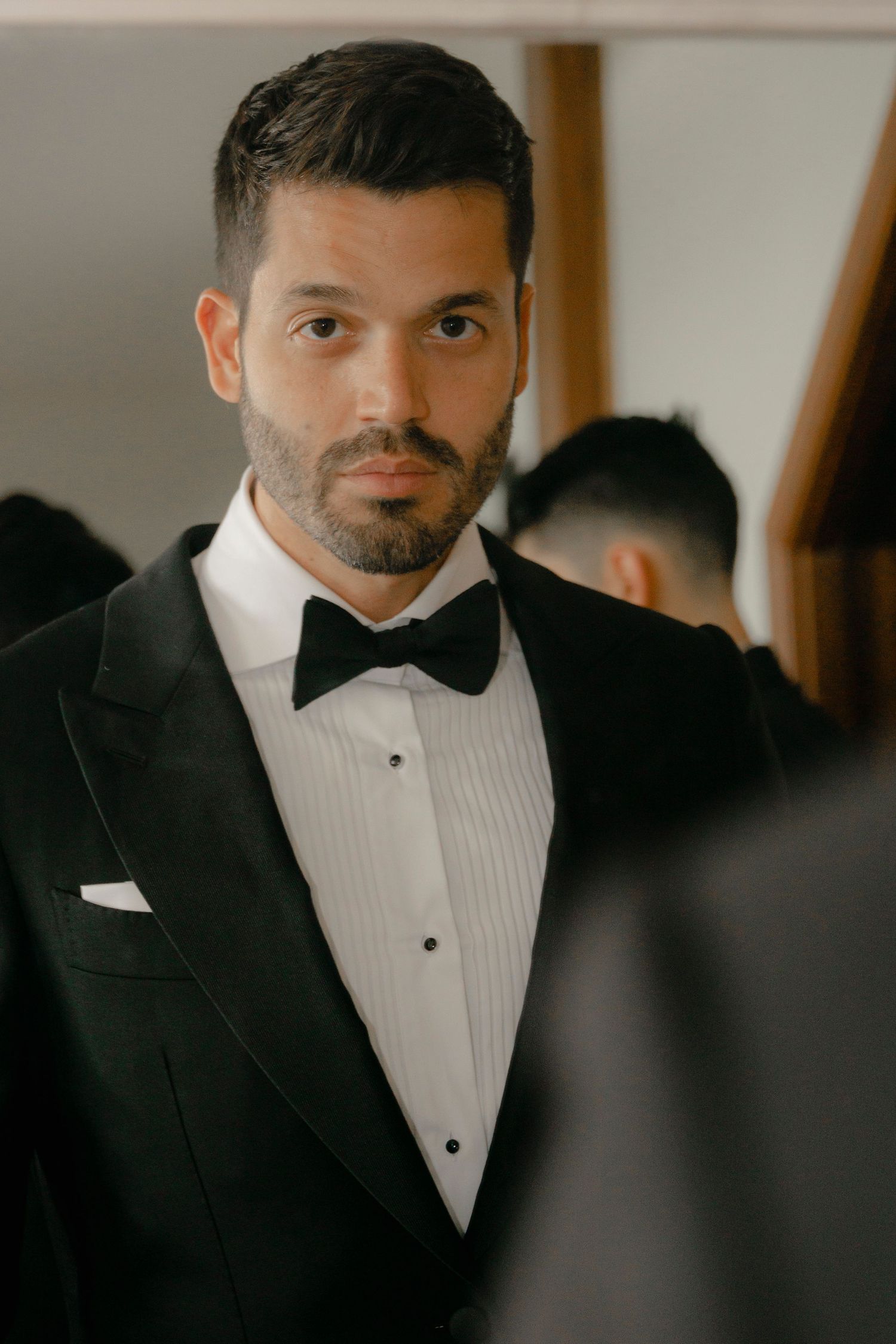 Man in black tuxedo and bow tie getting ready for formal event.