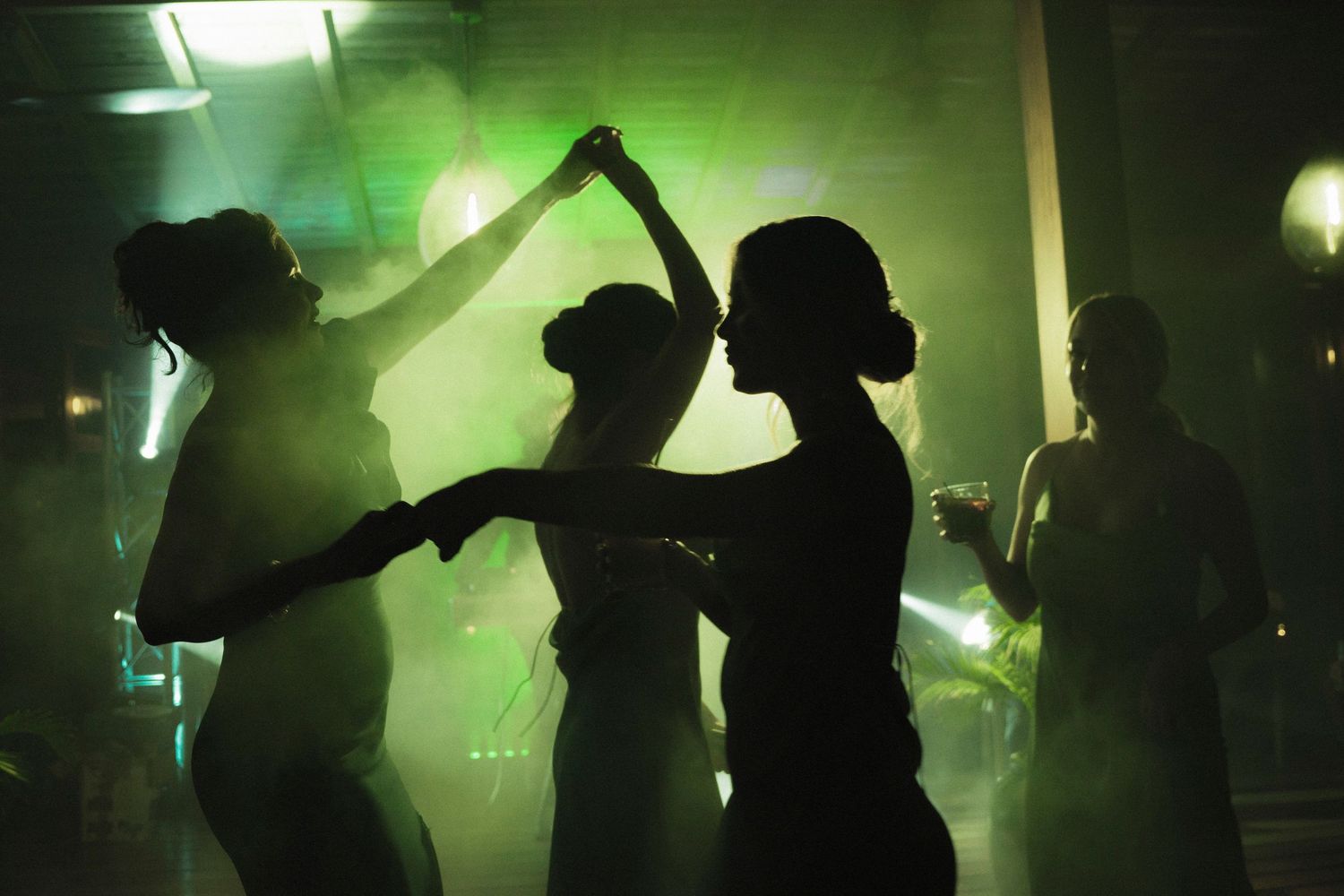 Silhouettes of people dancing in a nightclub with green lighting effects.