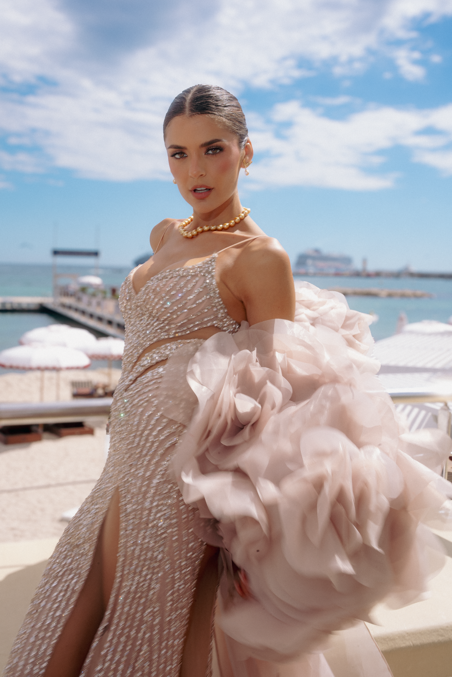 Luxurious blush pink gown with pearl details and dramatic ruffles against ocean backdrop.