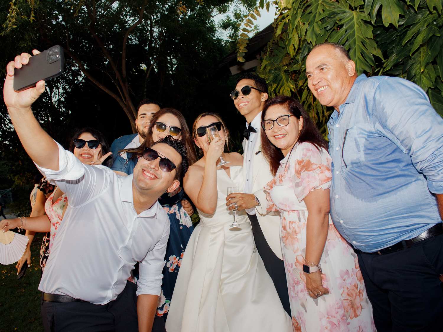 Wedding party enjoying candid moments outdoors with tropical landscaping.