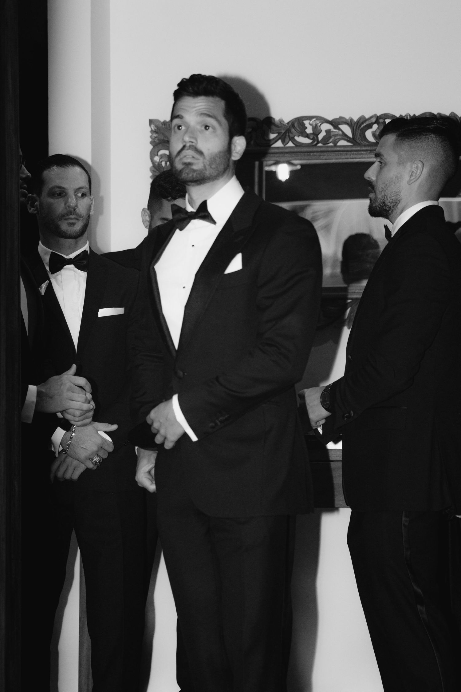 Group of men in black tuxedos and bow ties gathered for formal event.